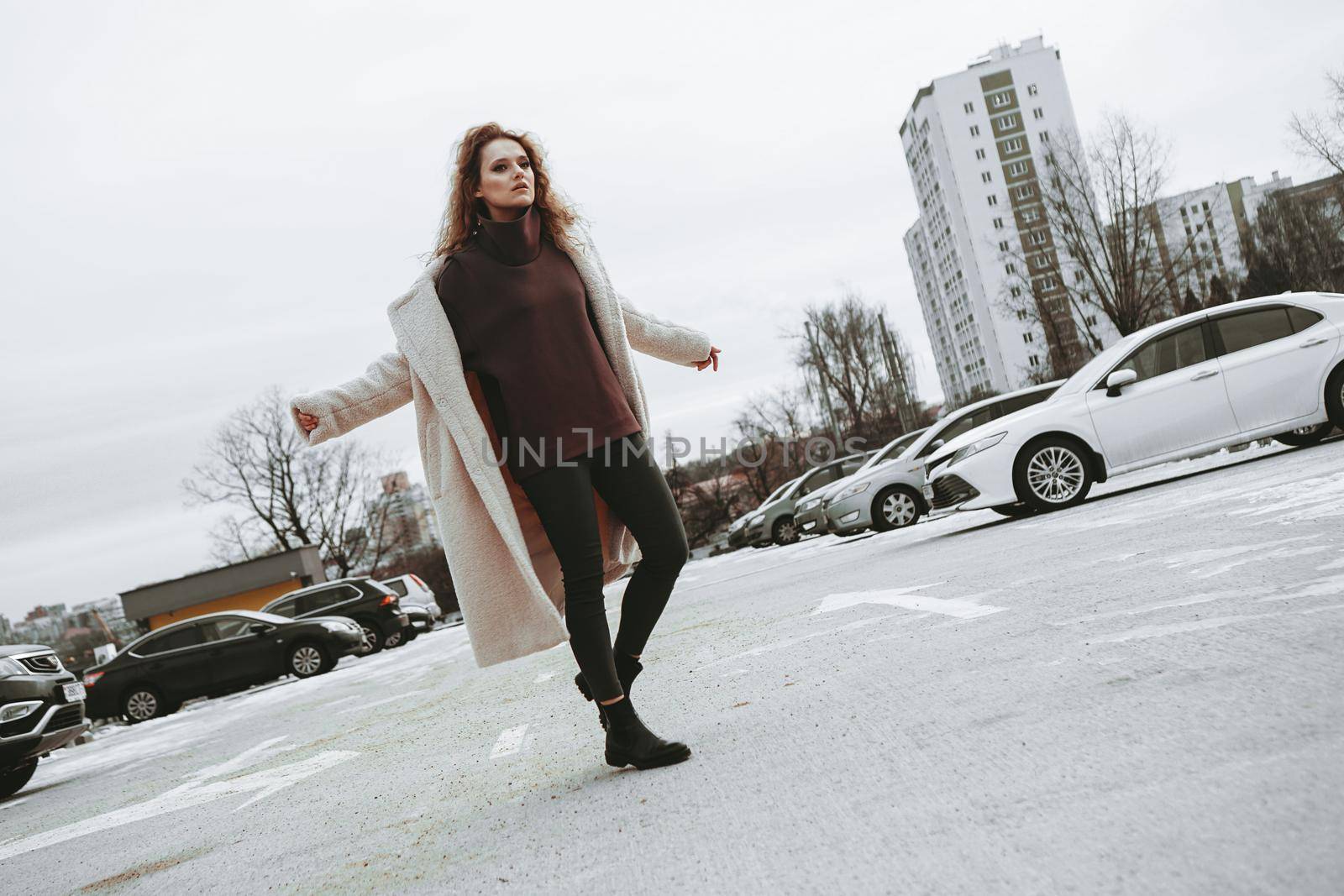 A girl with red curly hair in white coat poses on outdoor parking in cold autumn by natali_brill