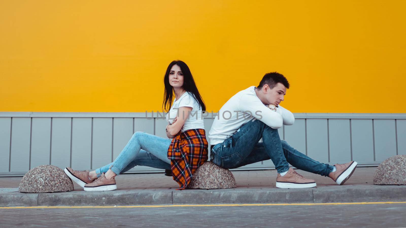 Confused young couple standing with one anothers back with crossed arms over yellow background