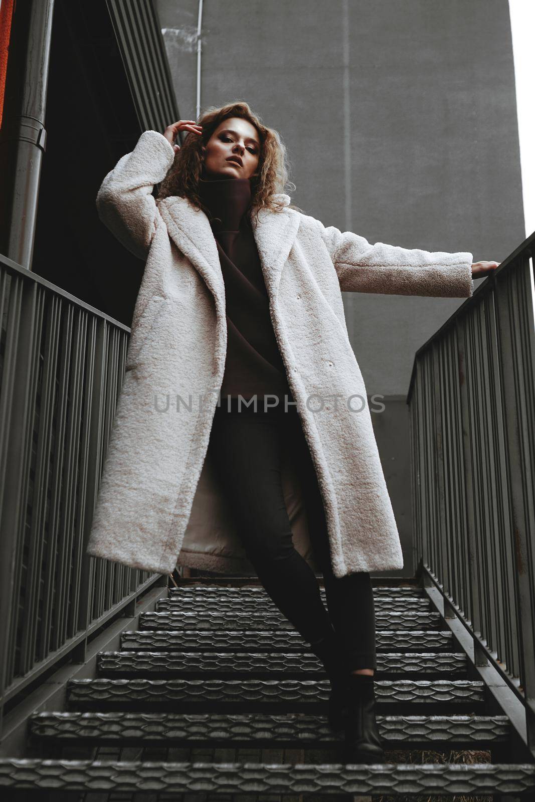 A girl with red curly hair in a white coat poses on the parking stairs by natali_brill