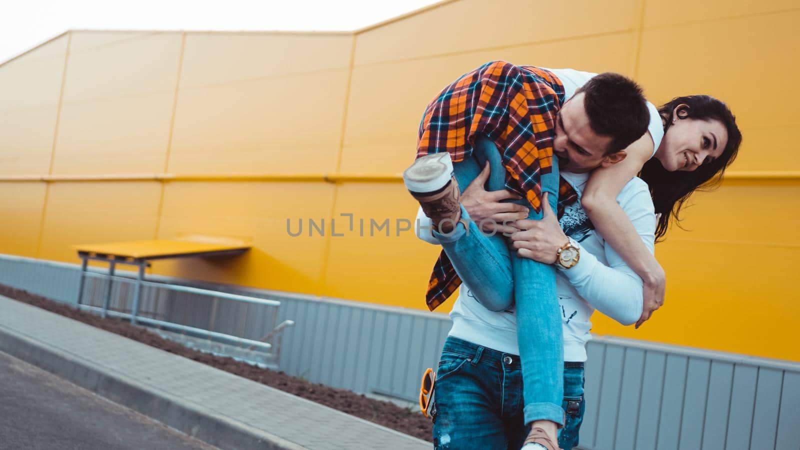 Happy man carrying his girlfriend on yellow background - couple in love