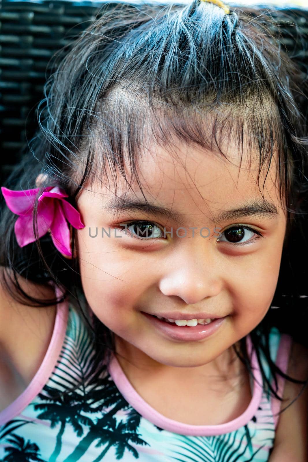 Little girl with large pink flower behind ear. Pretty asian child portrait with flower behind ear smiling by billroque