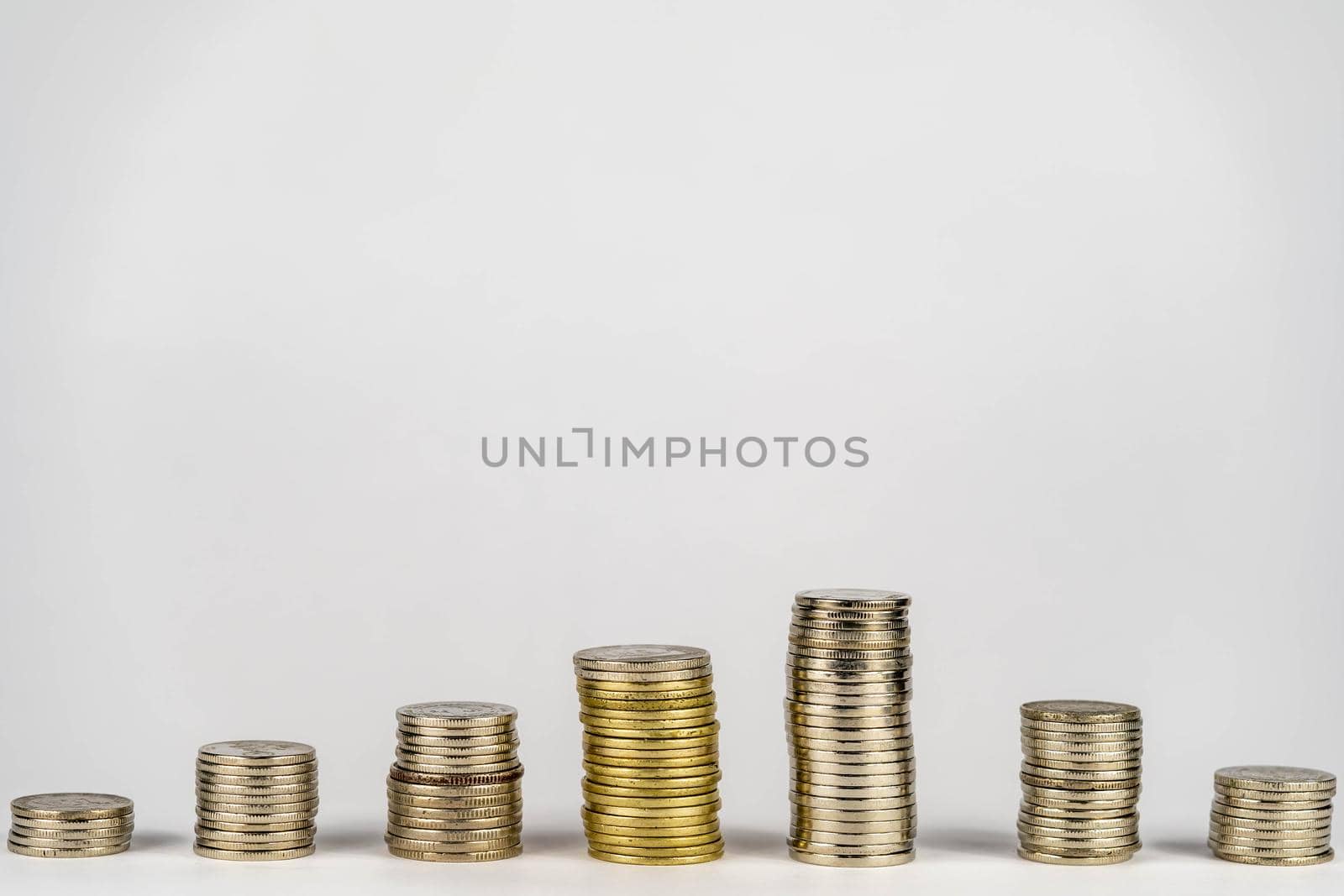 Seven stacks of golden coins with different heights arranged in growing direction, isolated on white background