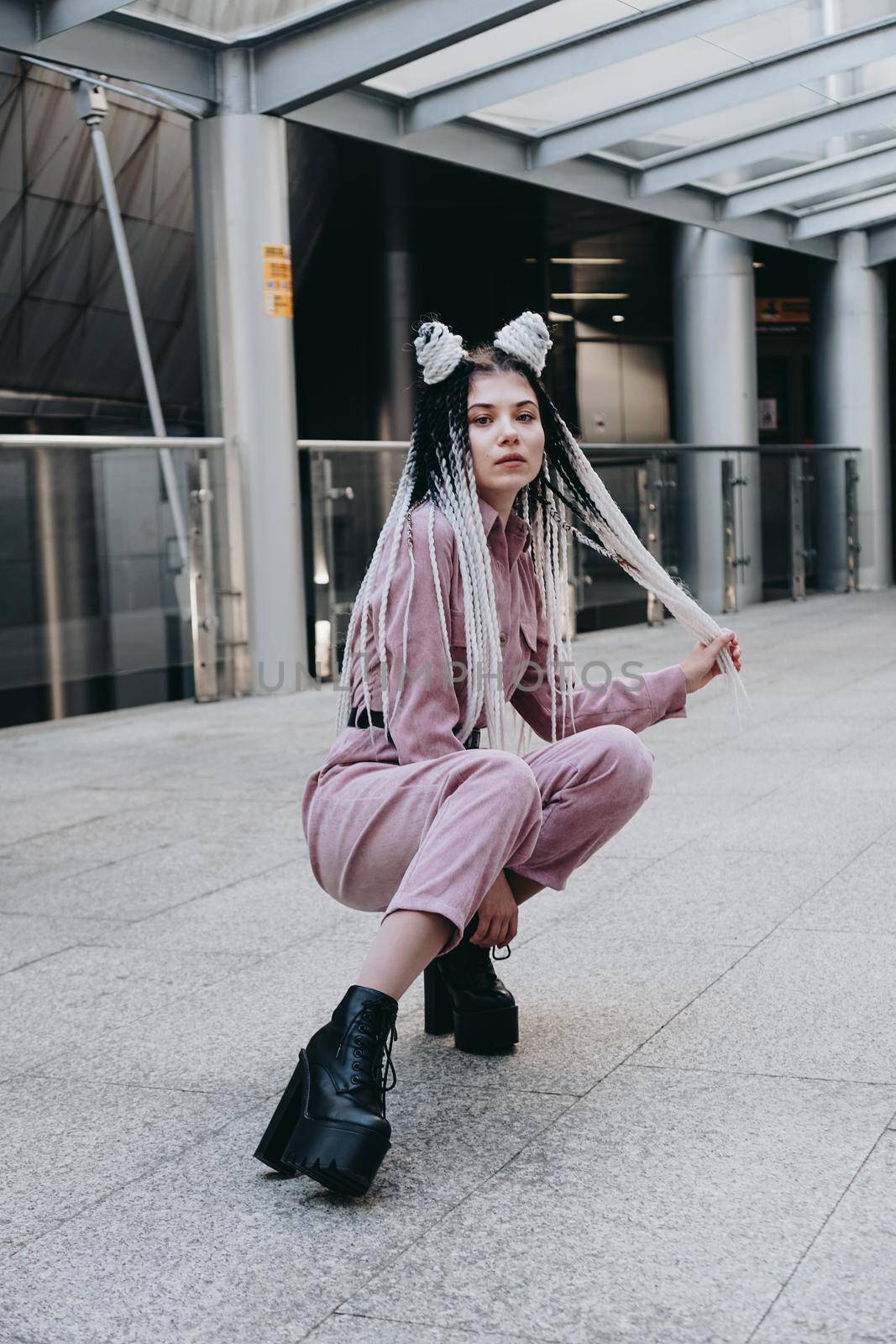 Young woman with futuristic looks. Girl with black and white dreadlocks or pigtails. Against the background of a futuristic building