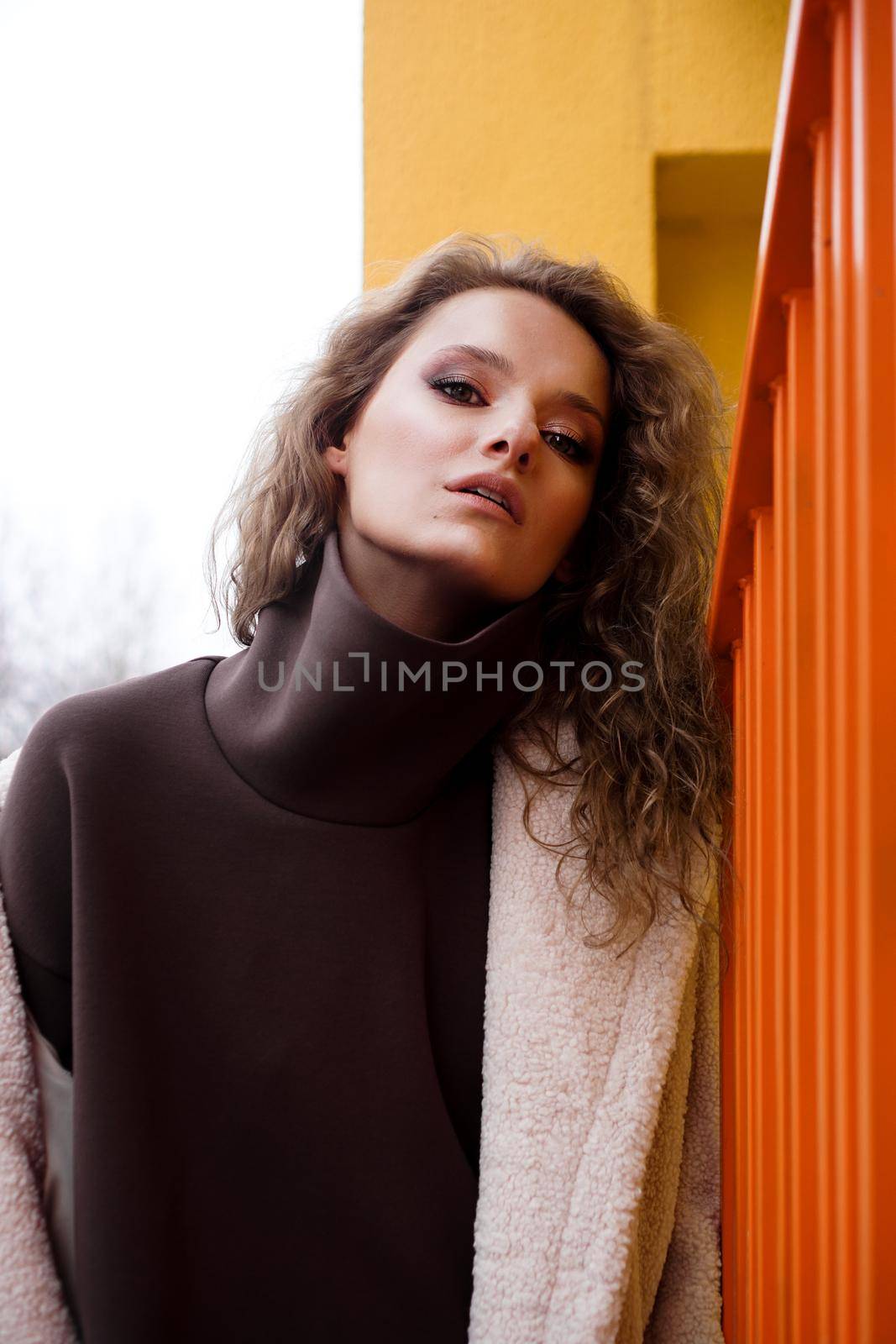 A girl with red curly hair in a white coat poses on the yellow parking stairs by natali_brill