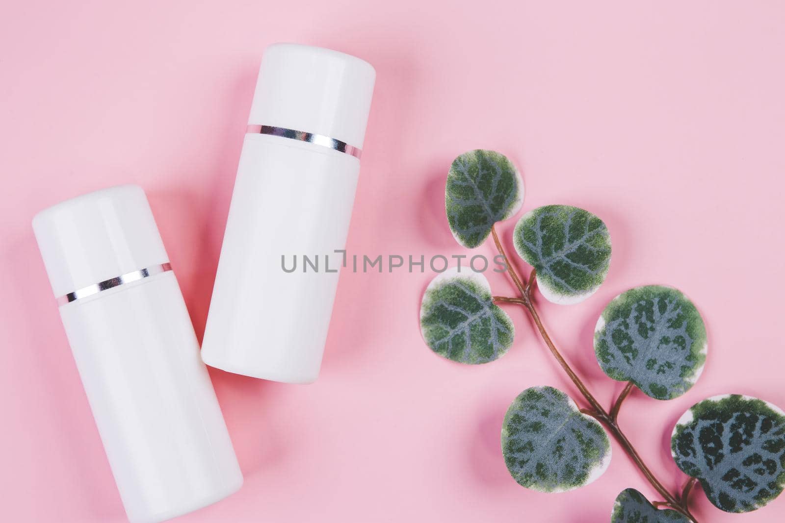 Mockup cosmetic bottle with cream or lotion and leaf isolated on pink background, mock up package for advertising, skincare or cosmetology, top view, flat lay, skin care and treatment with product.