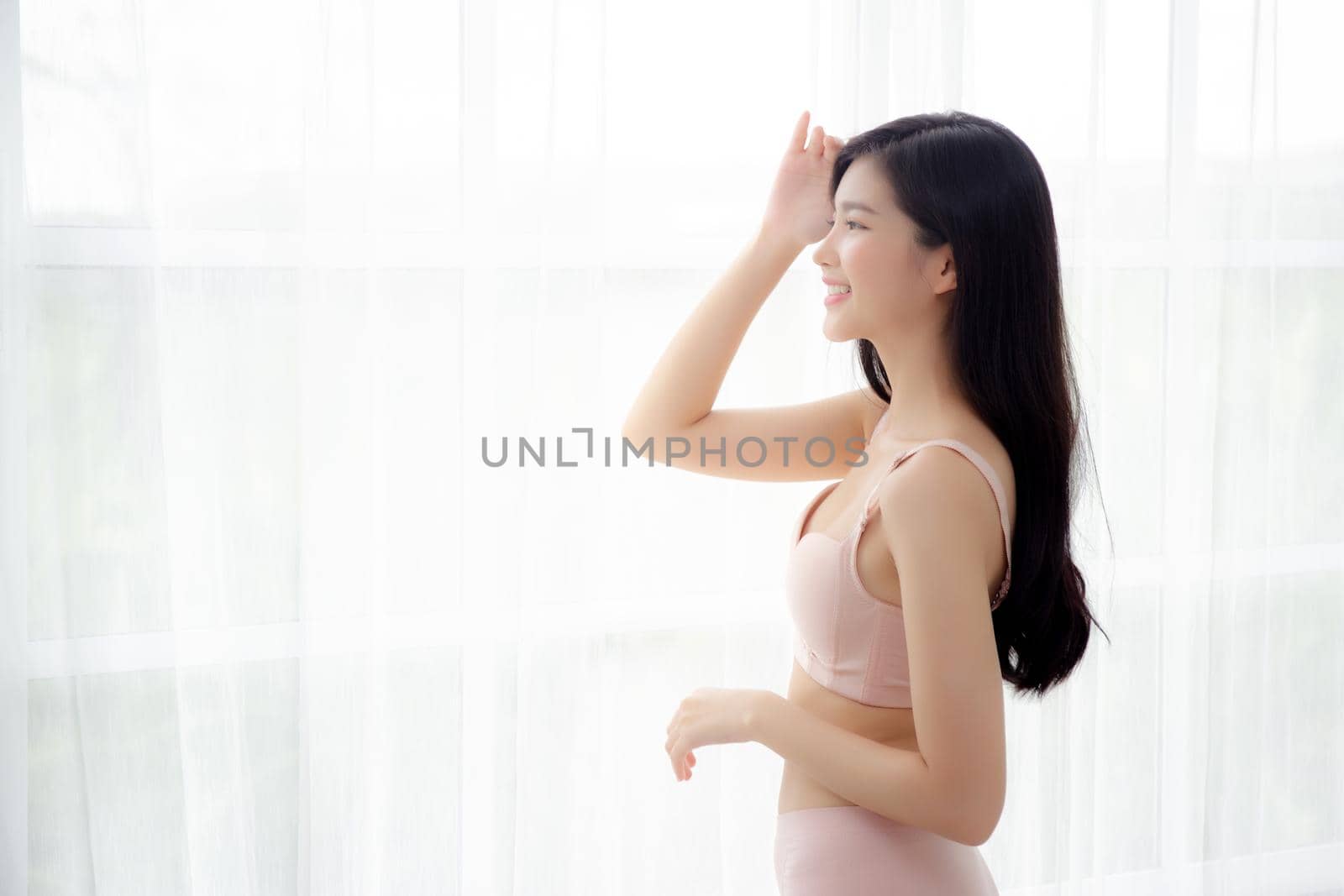 Beautiful portrait young asian woman sexy standing the window and smile while wake up with health, body of girl happy with freshness and cheerful with wellbeing, lifestyle and relax concept.