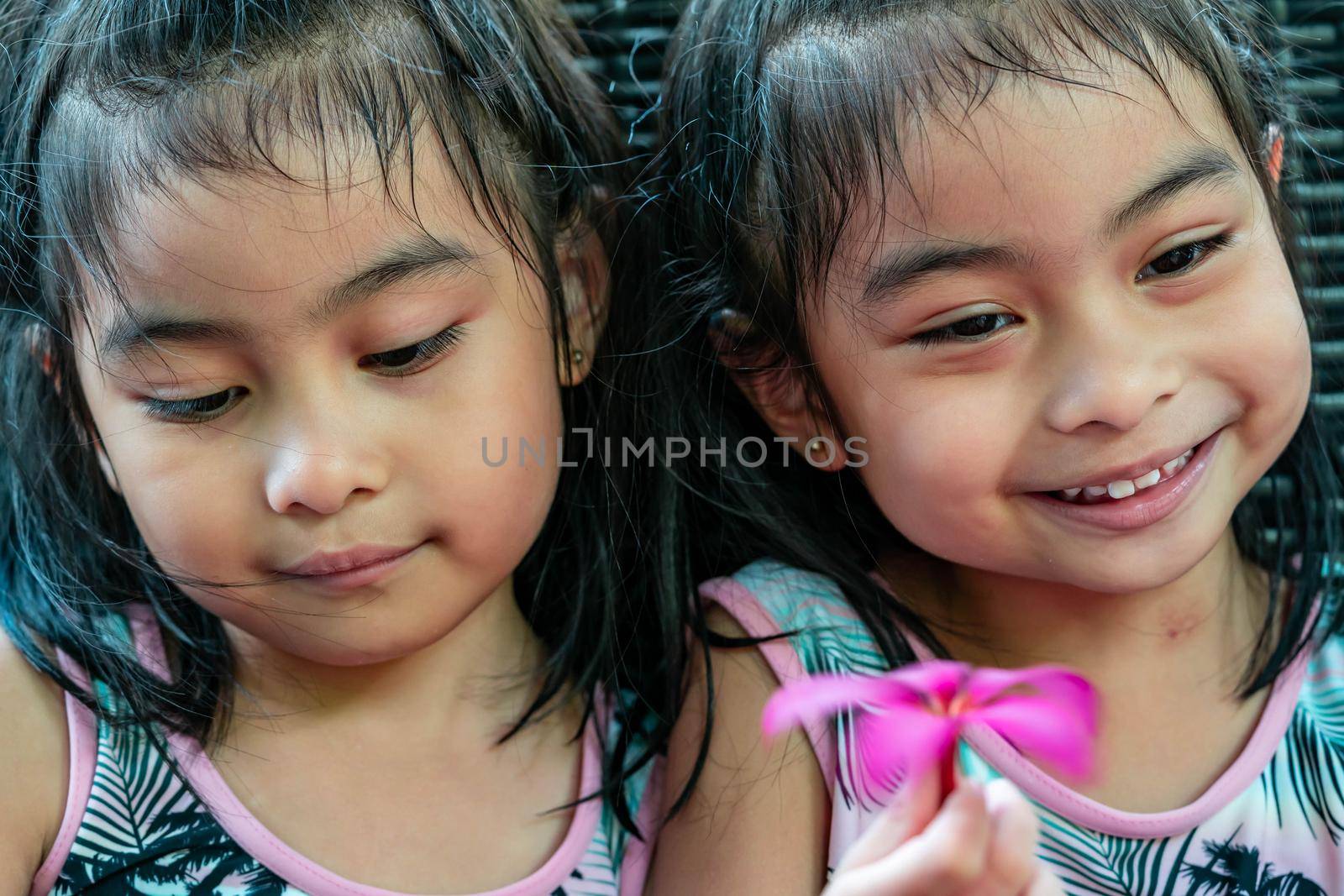 Pretty child twins holding a pink flower. Pretty asian twins portrait with flower and smiling by billroque