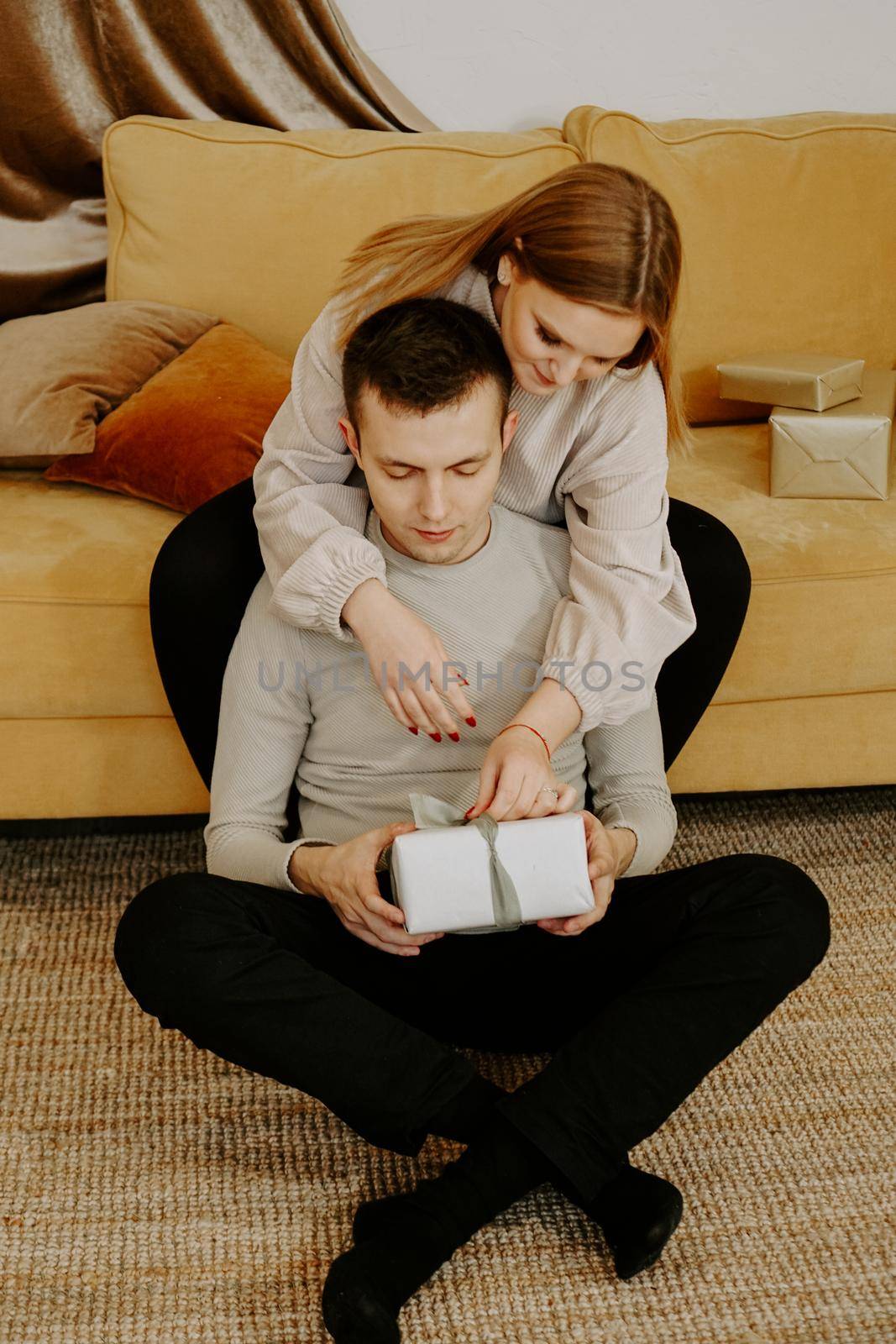 Beautiful young couple holding a gift box while sitting on couch at home - soft preset