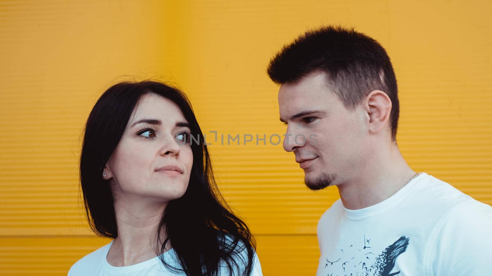Portrait of a cheerful young couple standing over yellow background - The guy looks at the girl, the girl looks into the distance
