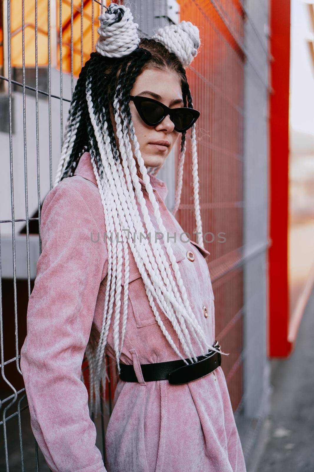 Portrait of beautiful cool girl over urban wall. Sunny day. Girl in sunglasses and pink jumpsuit