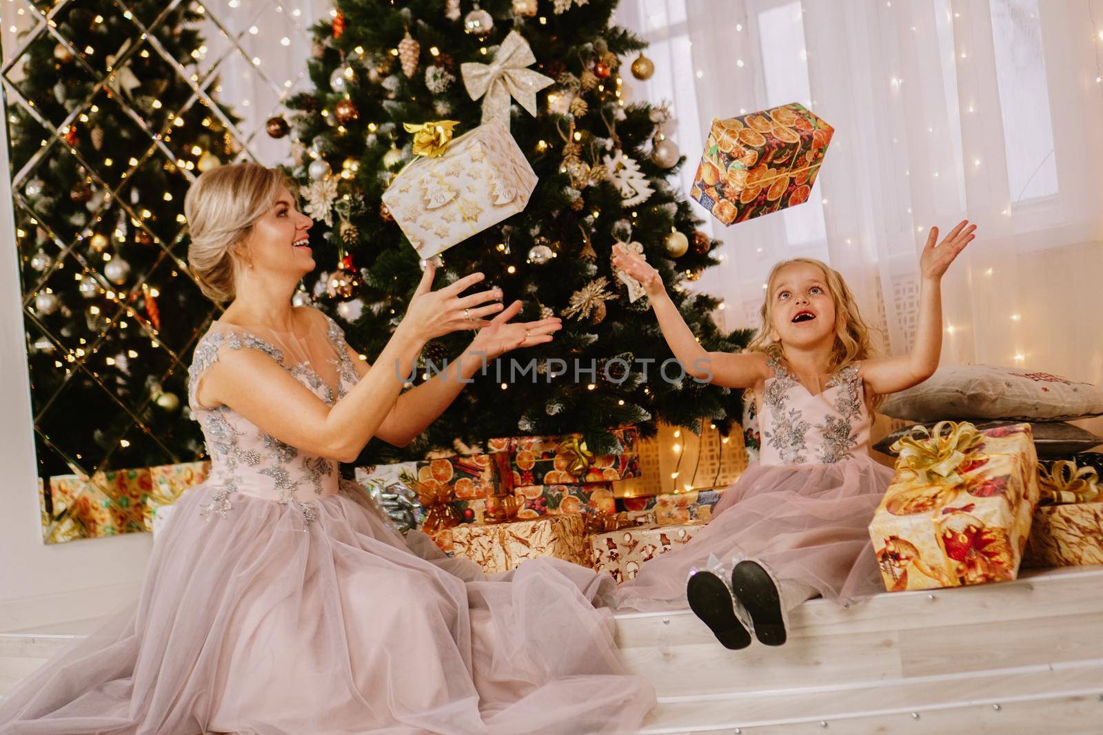 Happy mother and daughter sitting near christmas tree and throwing up gift boxes