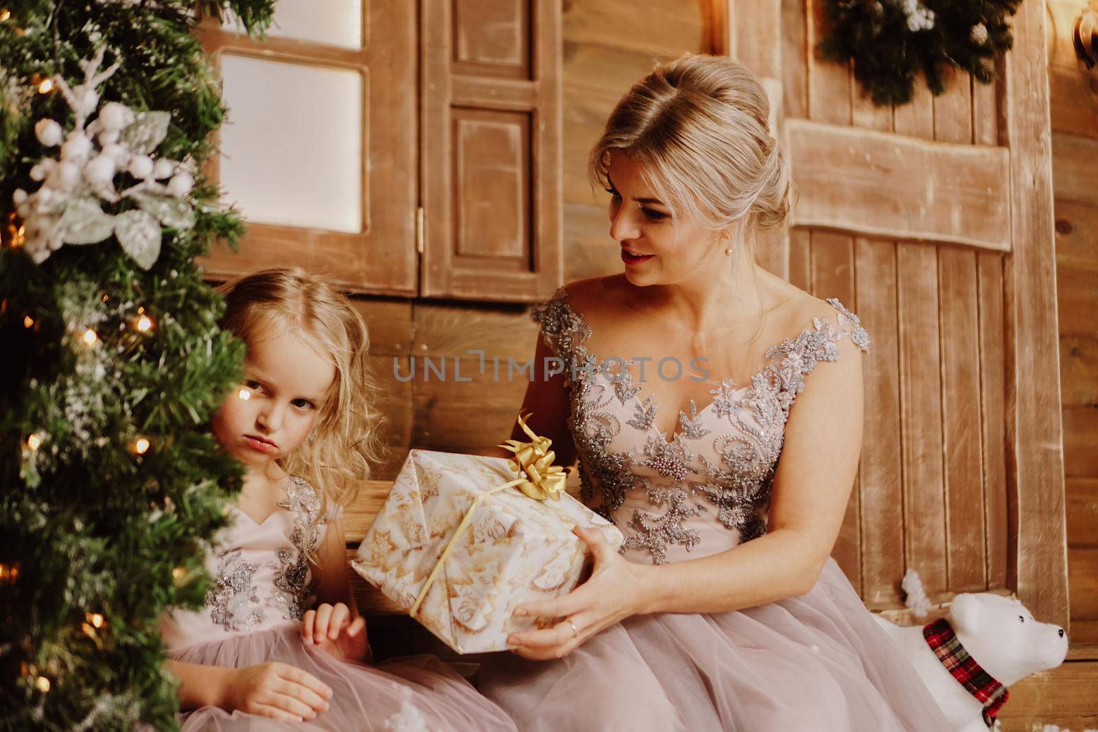 Mother calming down her sad crying infant daughter and gives her a present - standing by the Christmas tree