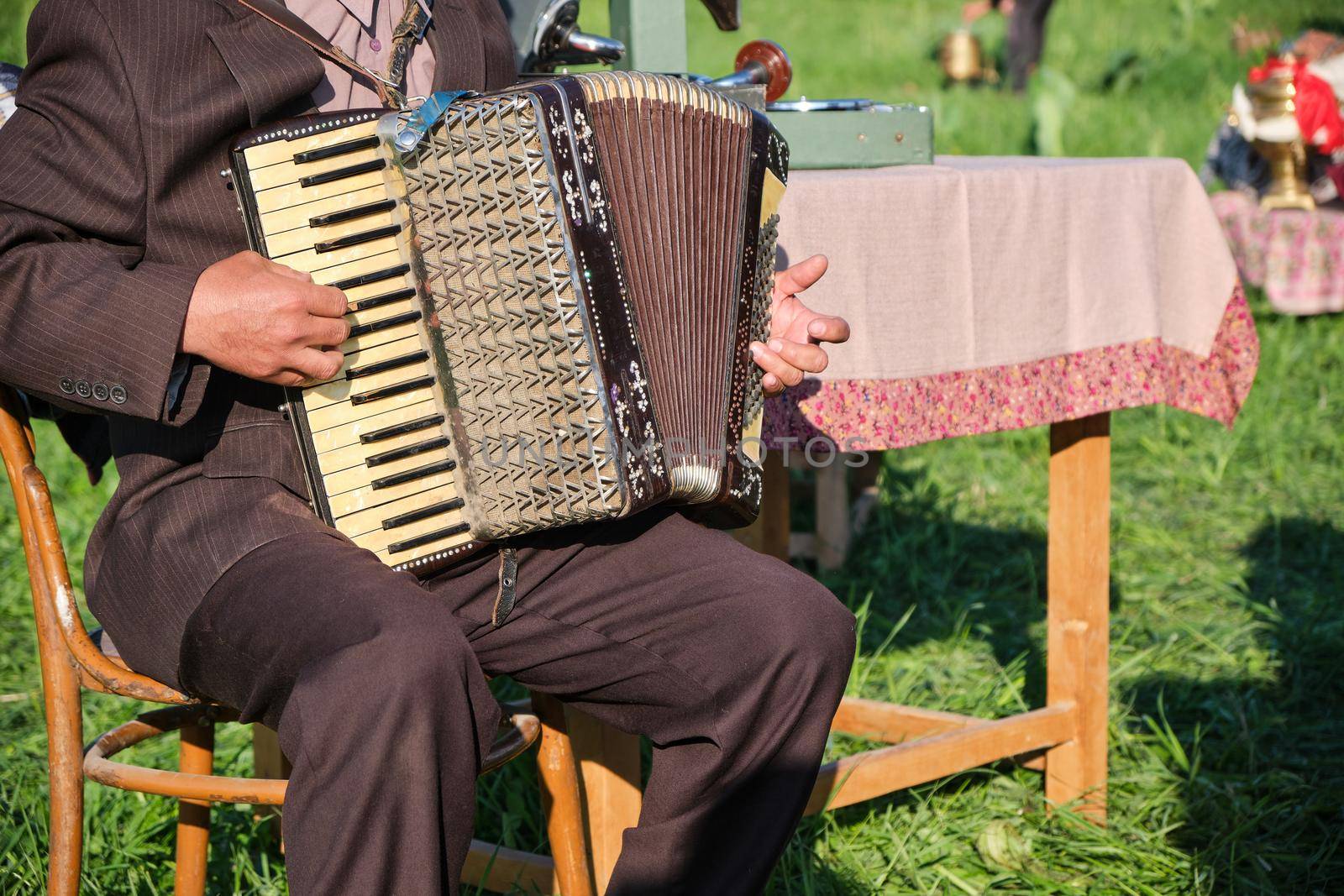 A musician sits on a chair and plays the accordion on a nature party.