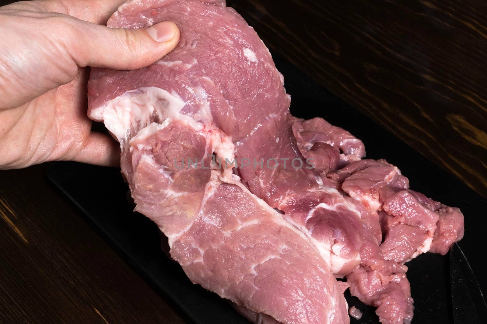 Slice the pork or beef with a knife on the table in close-up. Preparation of meat dishes and food products. Pieces of red meat for shish kebab, barbecue or kebab. Raw fresh meat