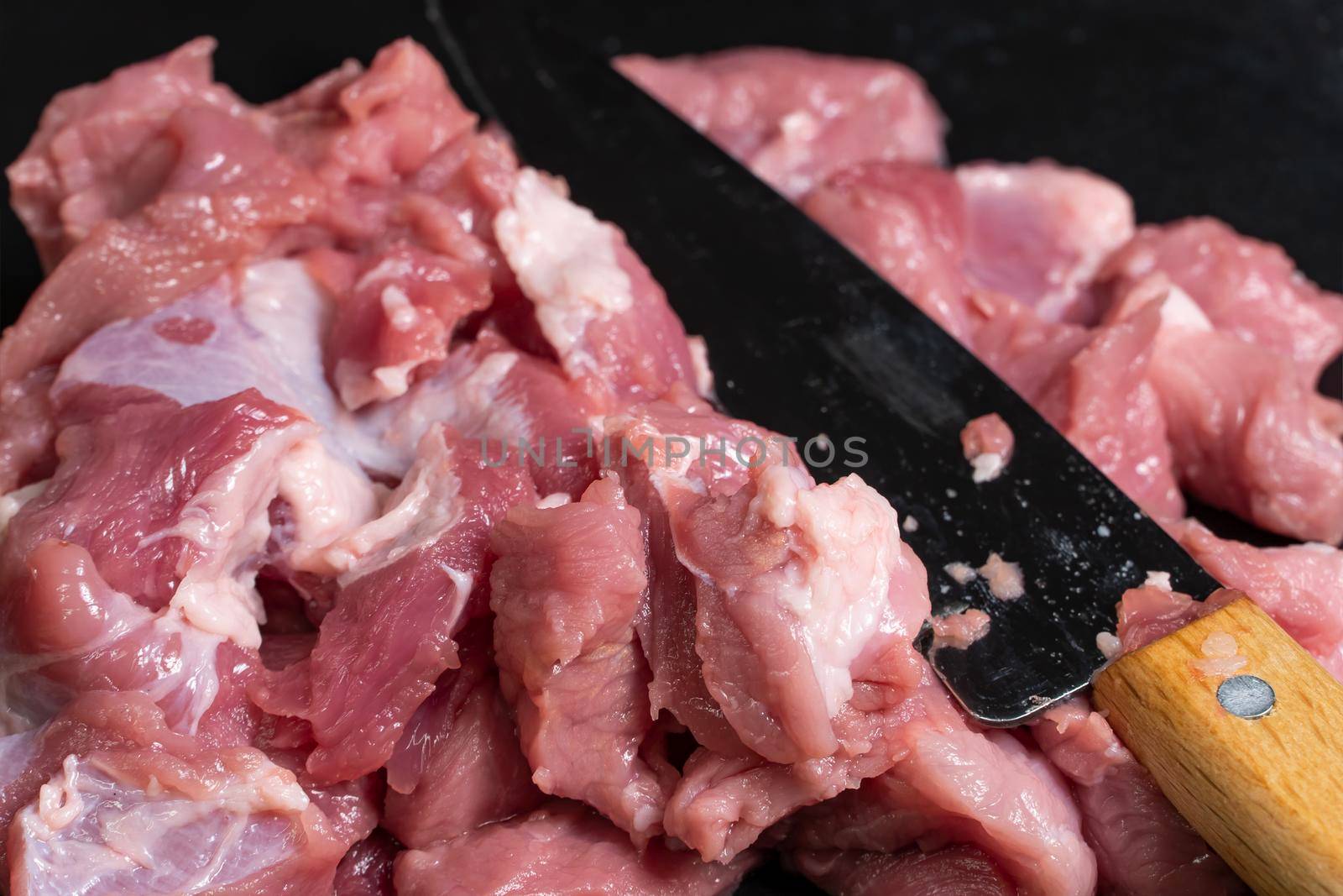 Slice the pork or beef with a knife on the table in close-up. Preparation of meat dishes and food products. Pieces of red meat for shish kebab, barbecue or kebab. Raw fresh meat is cut with a knife