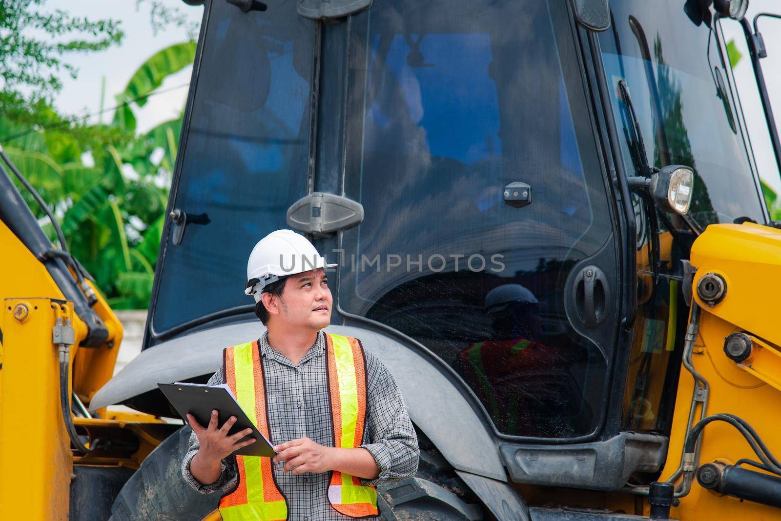 Asian man civil construction engineer worker or architect with helmet and safety vest working and holding a paper board note for see blueprints or plan at a building or construction site