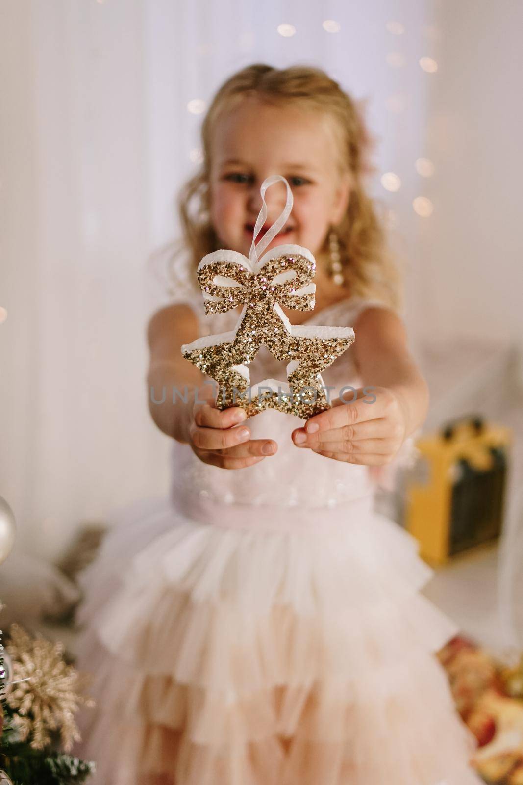 Little cute girl with a Christmas star in her hands smiling on the background of Christmas decor.