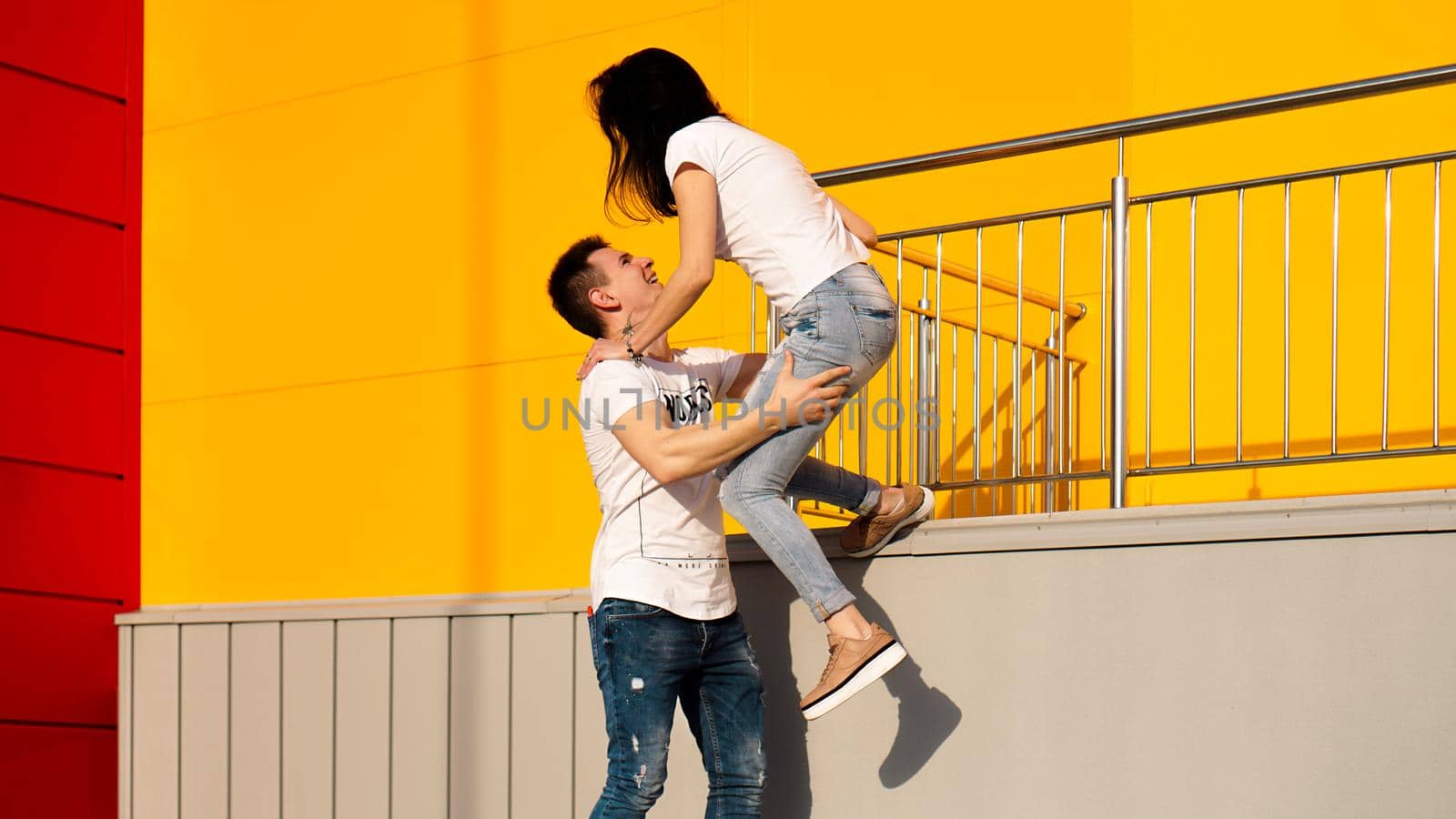 Happy man carrying his girlfriend on yellow background - couple in love