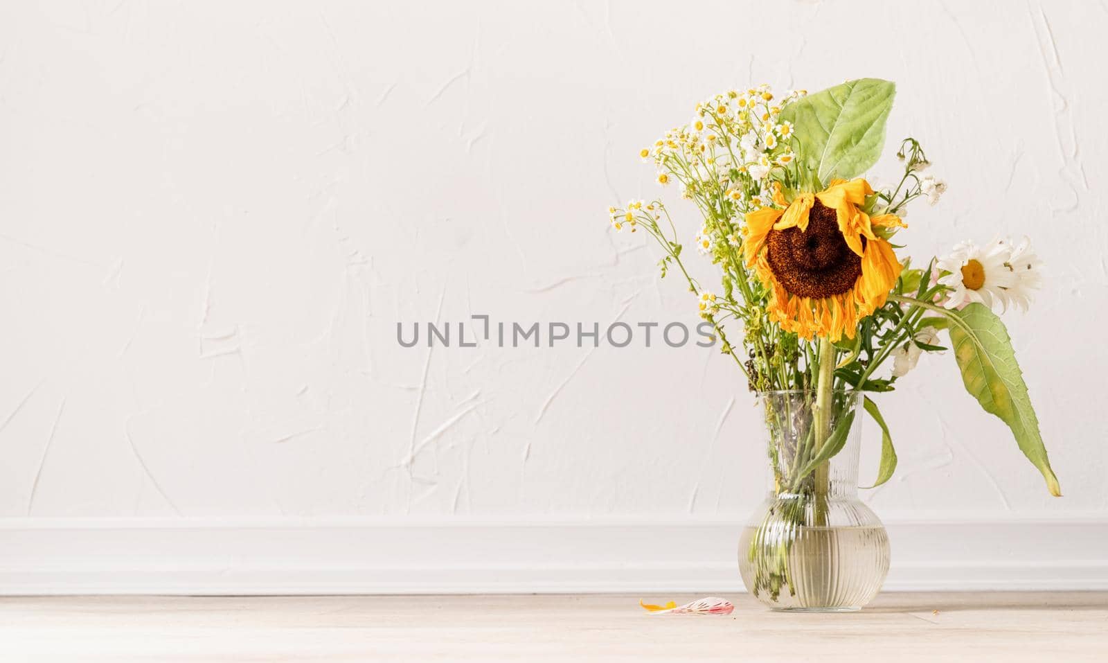 Autumn concept. A bouquet of withered flowers and a sunflower in a vase
