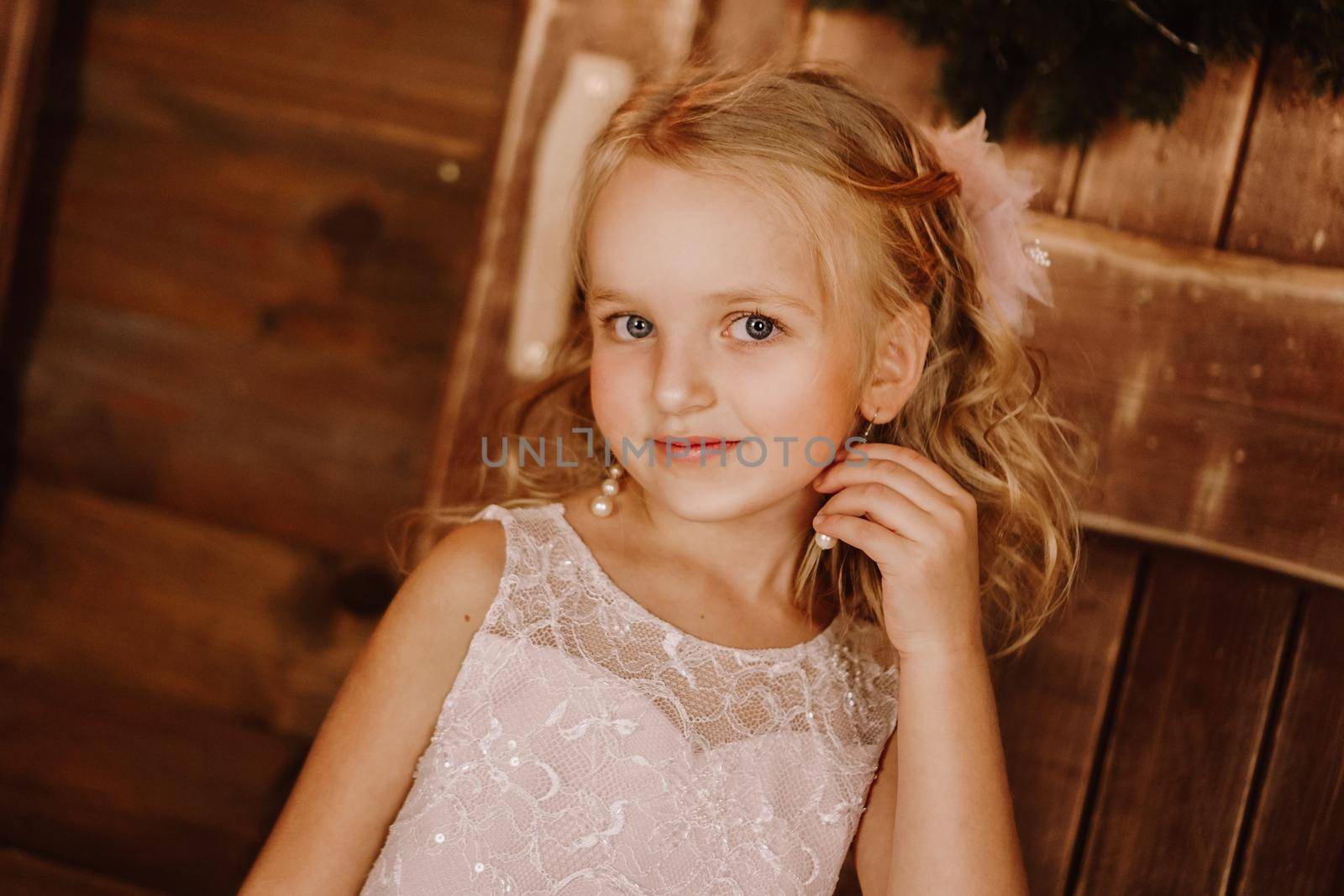 Girl with long blond hair fix earring from pearls in pink dress on wooden background