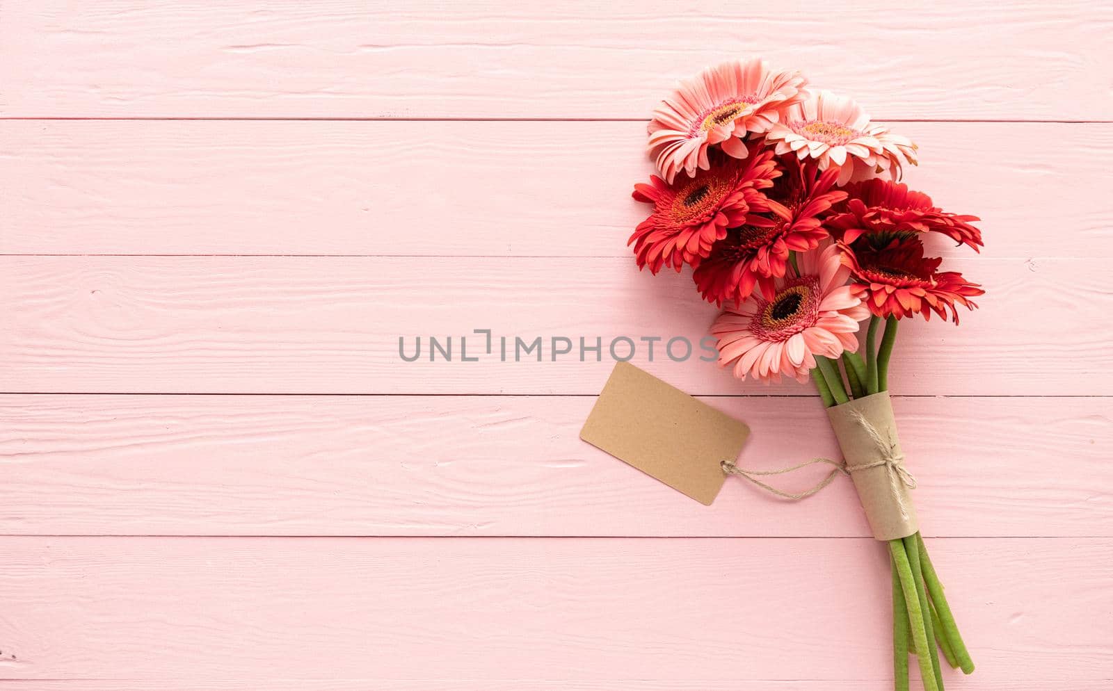 Happy birthday. Red gerbera daisy flowers and blank craft label tag on pink wooden table, flat lay