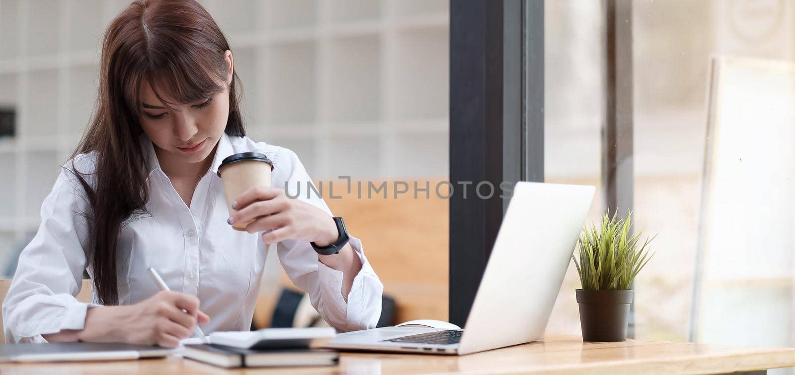 Woman having a tea, sitting on a floor in an office, writing down notes, opened laptop in front of her. Home office concept. by wichayada