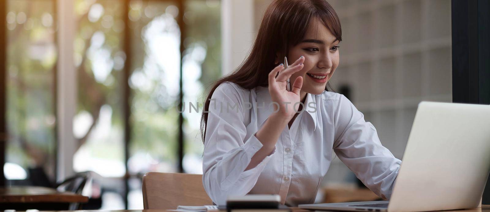 Portrait of a beautiful young woman studying while sitting at the table with laptop computer and notebook at home by wichayada