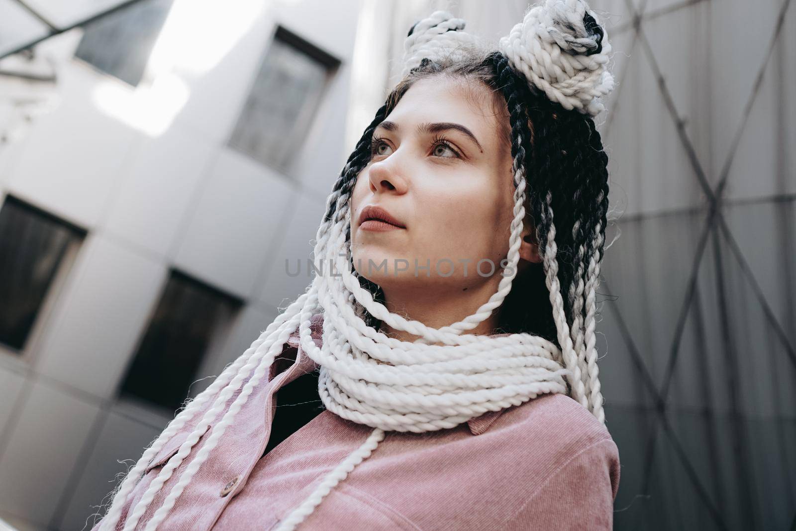 Young woman with futuristic looks. Girl with black and white dreadlocks or pigtails. Against the background of a futuristic building