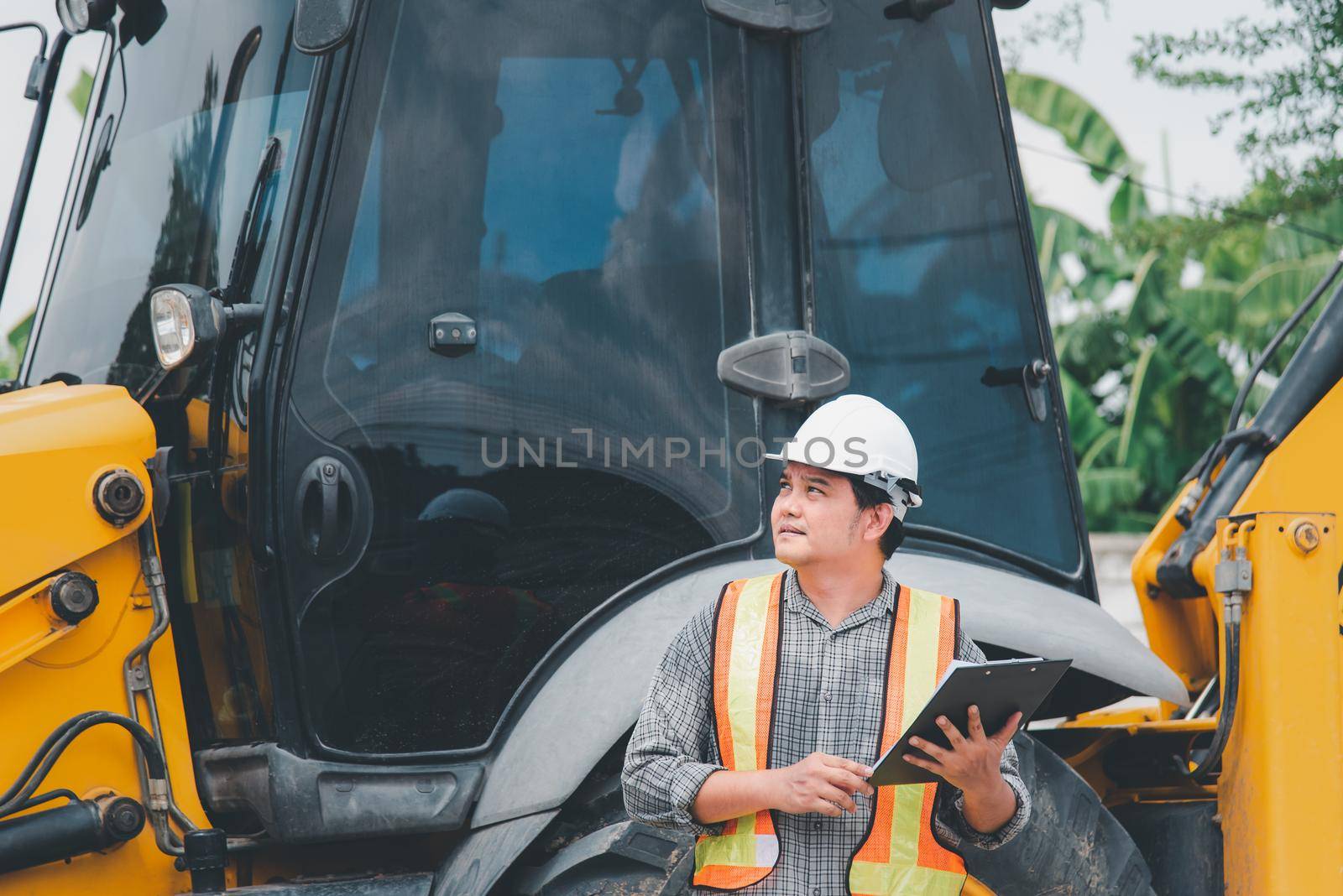 Asian man civil construction engineer worker or architect with helmet and safety vest working and holding a paper board note for see blueprints or plan at a building or construction site