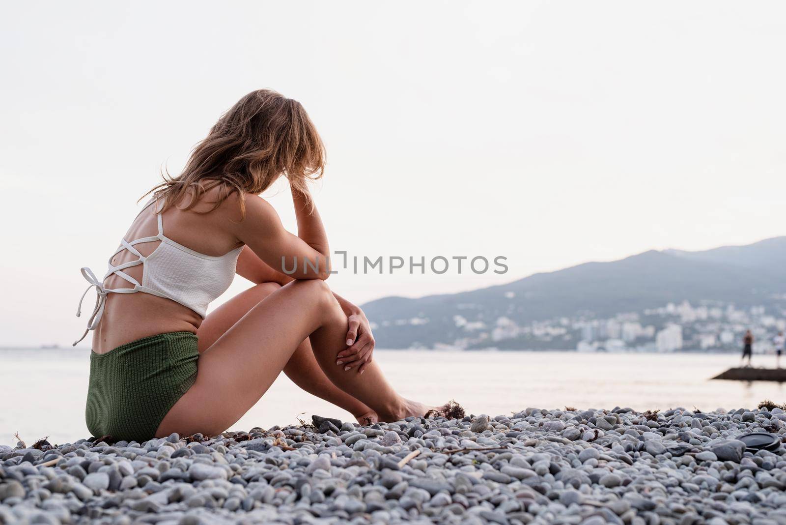 young depressed woman sitting on the beach looking away, rear view by Desperada