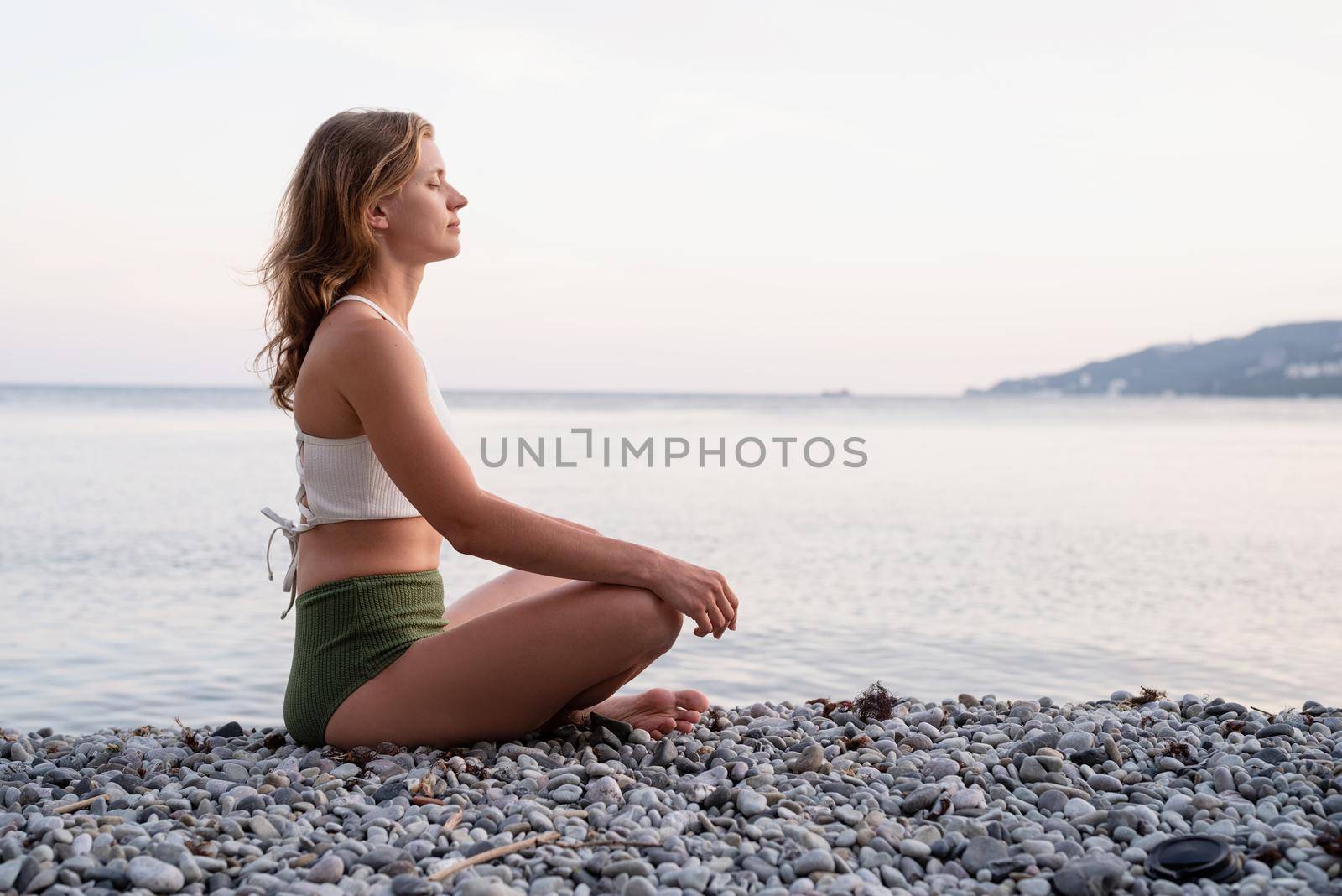 young woman meditating on the beach by Desperada