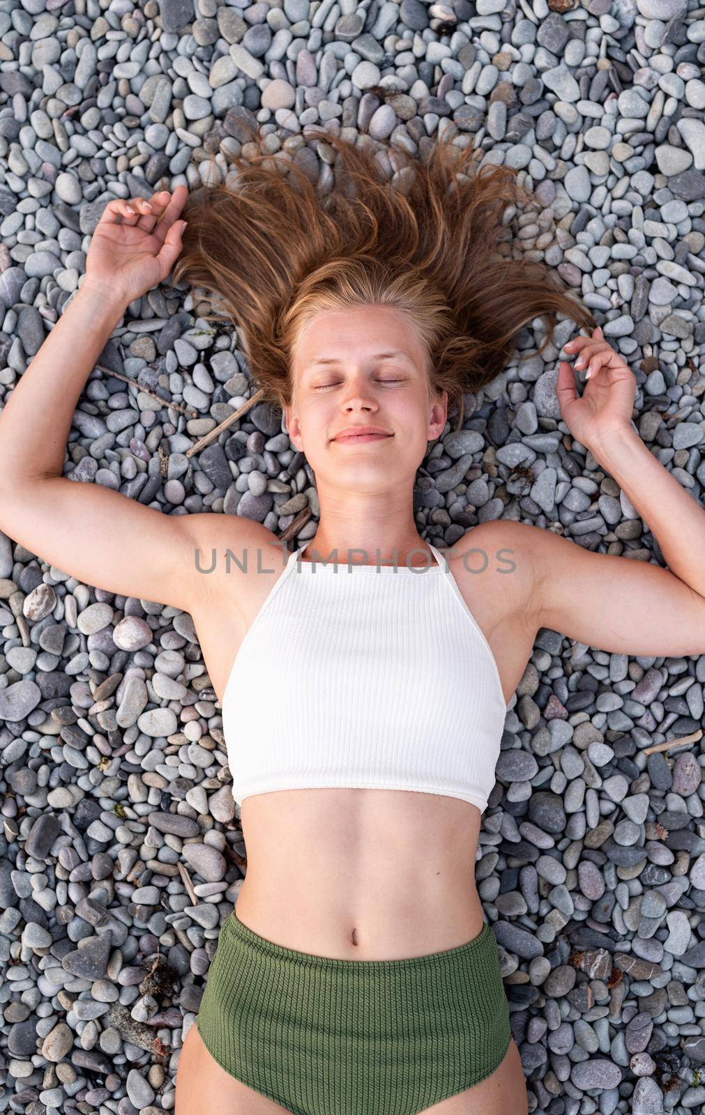 Summer vacation. Top view of young smiling woman in swimsuit lying on stone beach