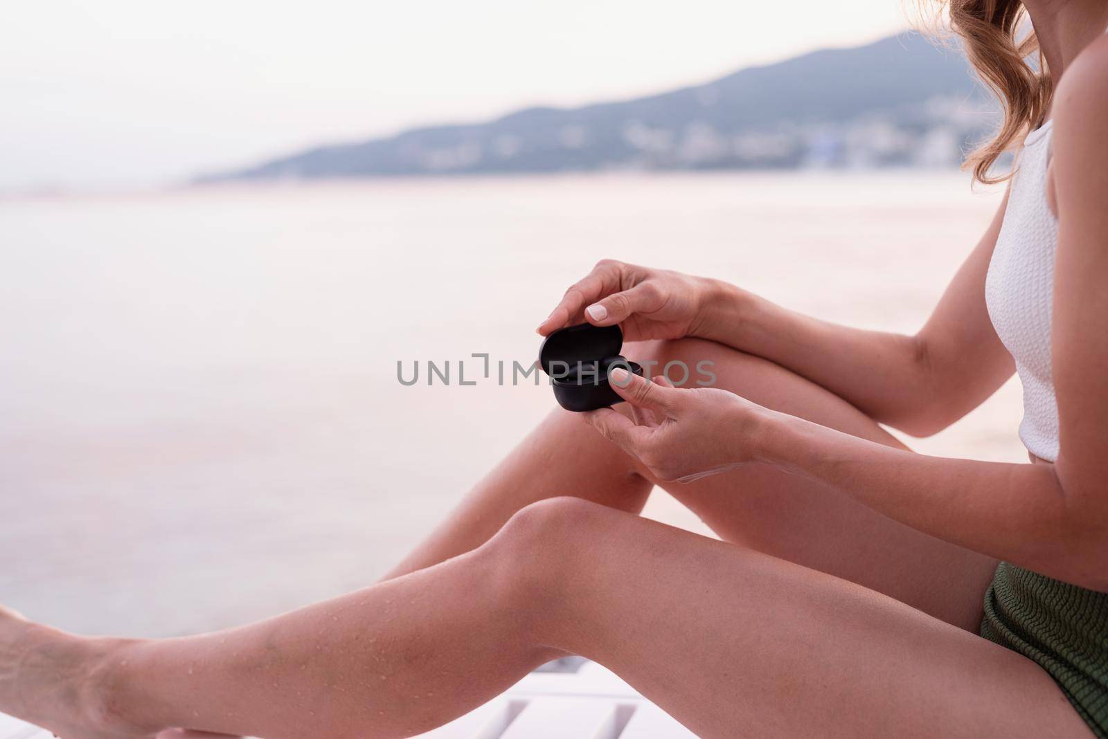 Woman sitting on the sun lounger opening a box with wireless earpieces, ready for listening to the music