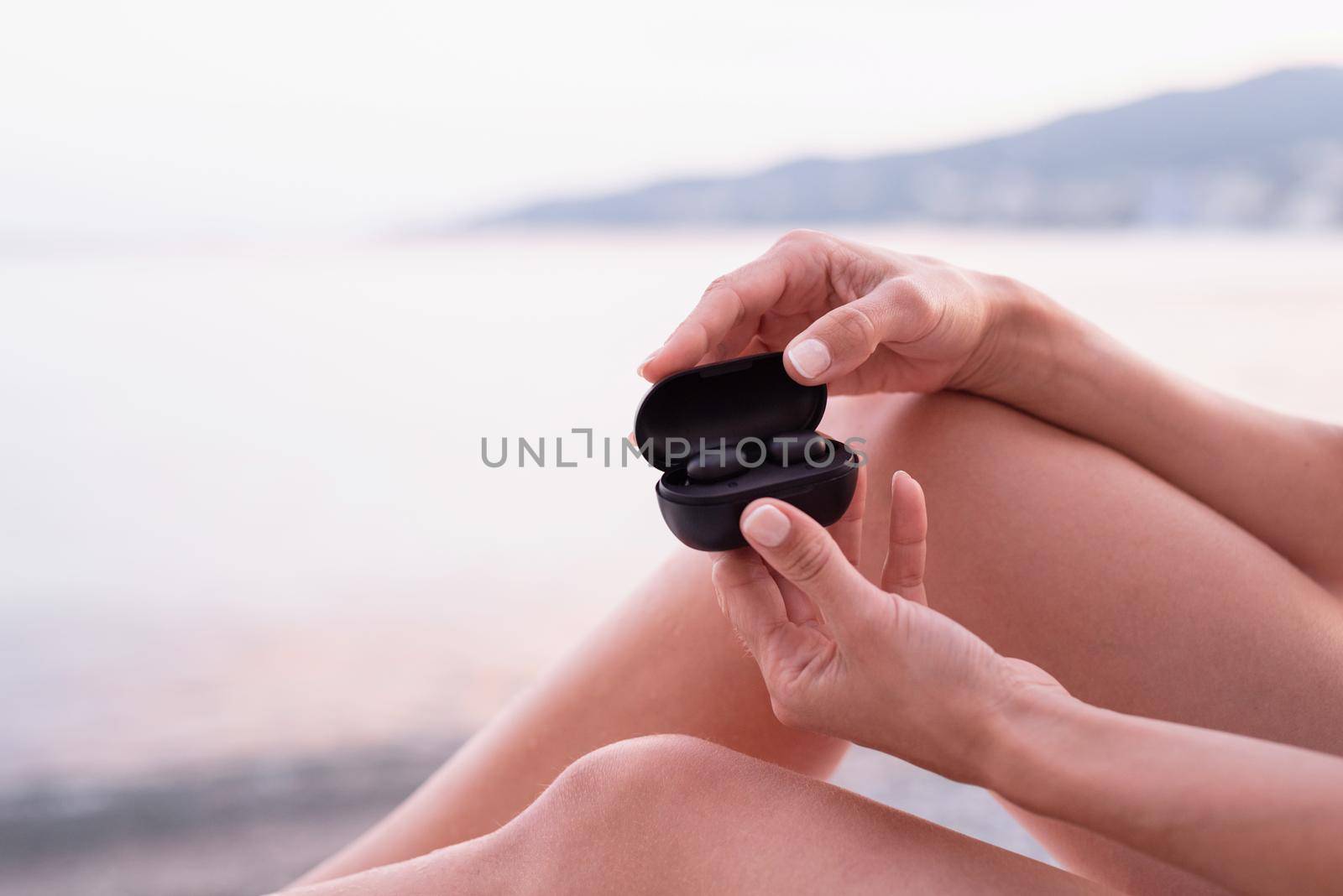 Woman sitting on the sun lounger opening a box with wireless earpieces, ready for listening to the music