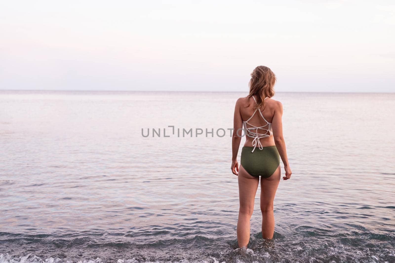 Rear view of a young woman standing on stony beach looking at the sea by Desperada