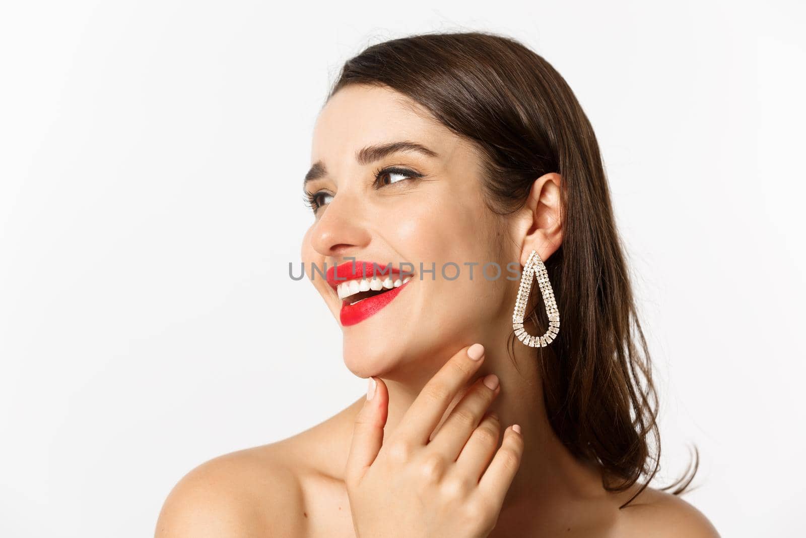 Fashion and beauty concept. Headshot of gorgeous brunette woman with red lipstick, earrings, laughing and looking left, standing over white background by Benzoix