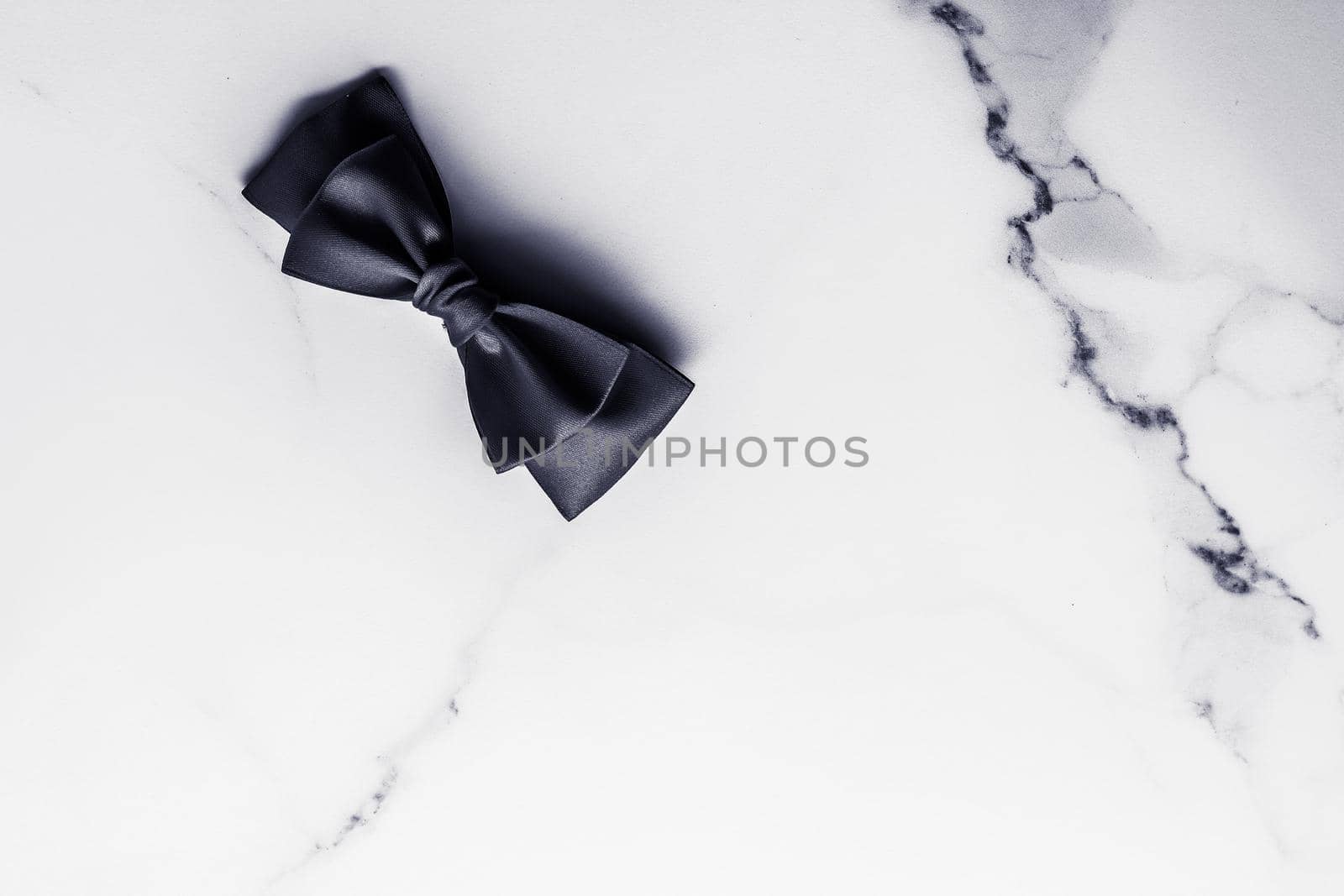 Black silk ribbon and bow on marble background, flatlay by Anneleven