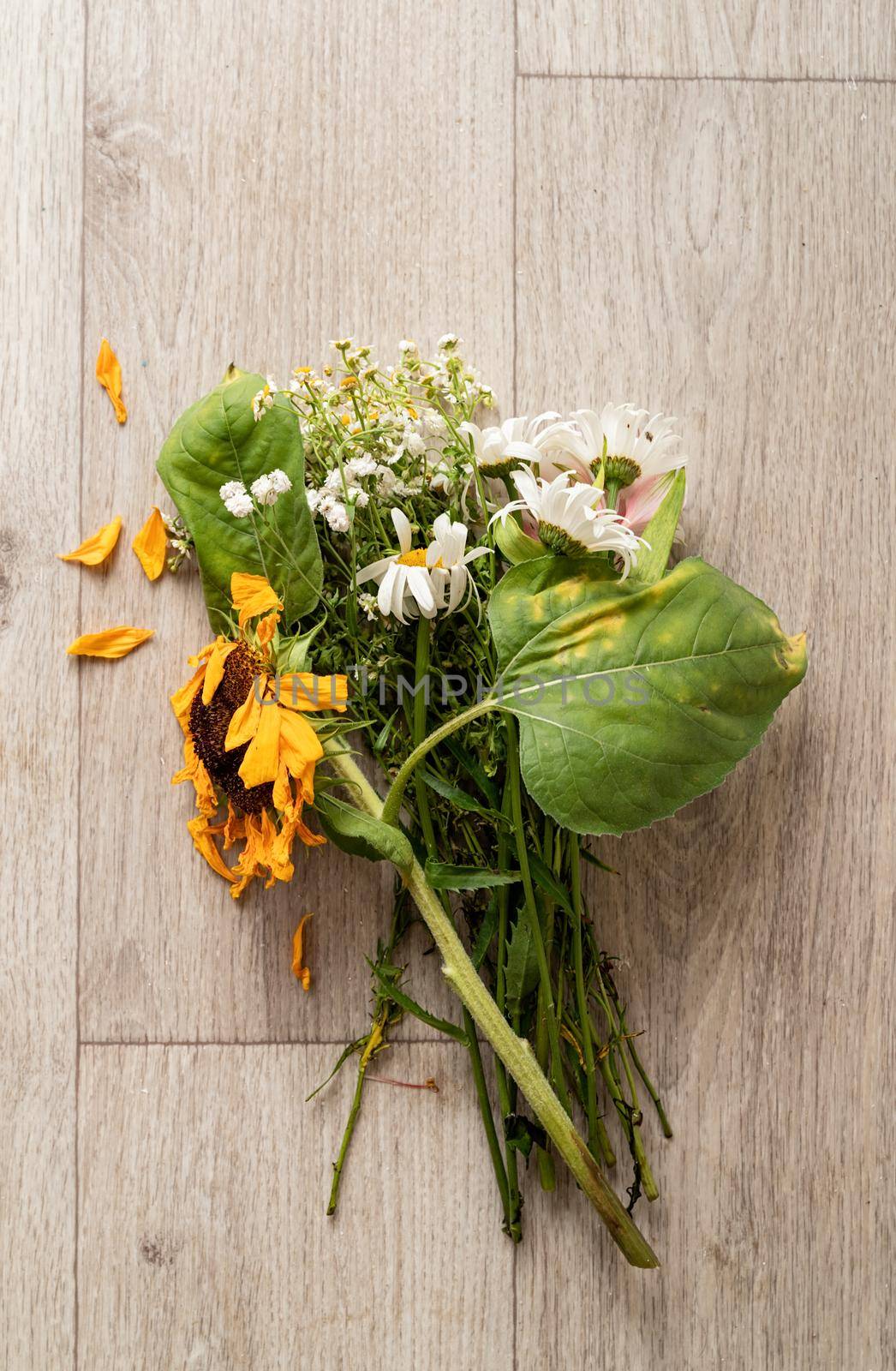 Autumn concept. A bouquet of withered flowers and a sunflower on the floor. Flat lay