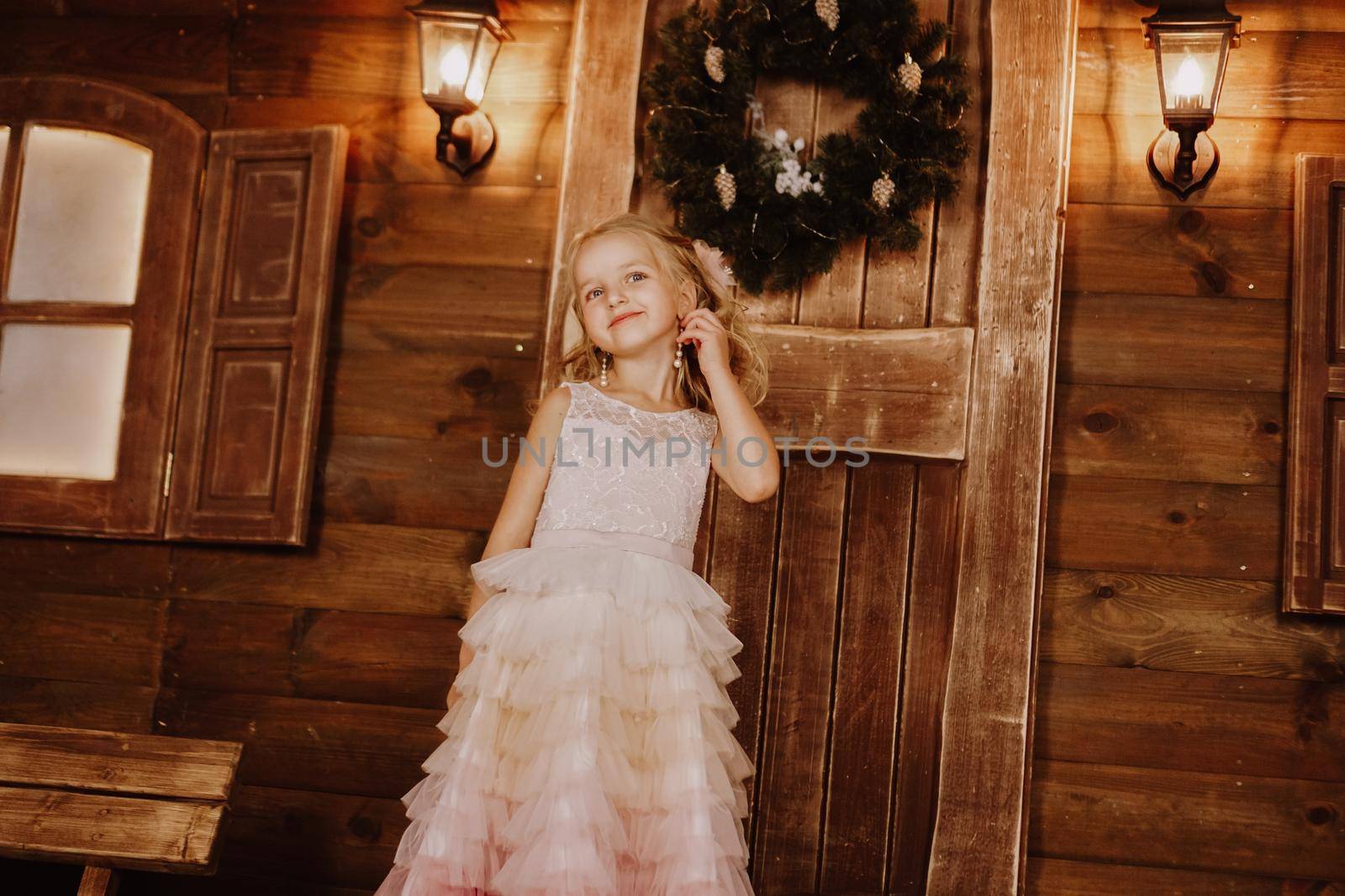 Girl with long blond hair fix earring from pearls in pink dress on wooden background. Christmas time