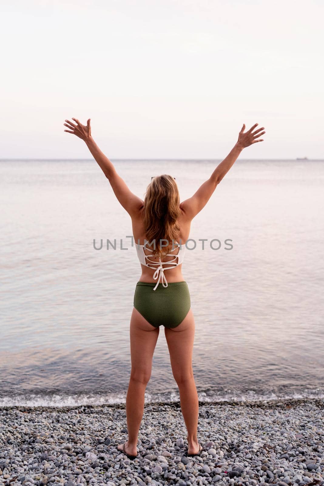 Summer vacation. Rear view of a young woman standing on stony beach with outstretched arms