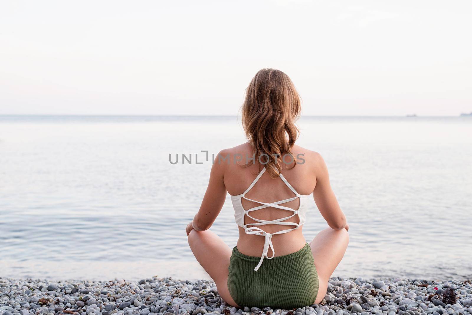Rear view of a young woman meditating on the beach by Desperada