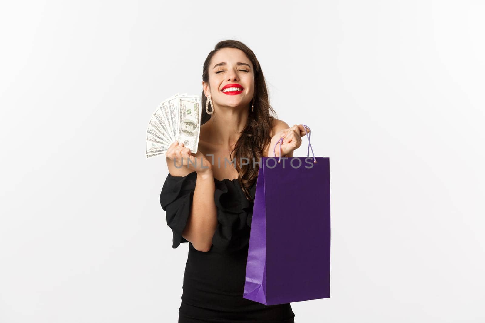 Satisfied and happy woman enjoying shopping, holding bag and money, smiling pleased, standing over white background.
