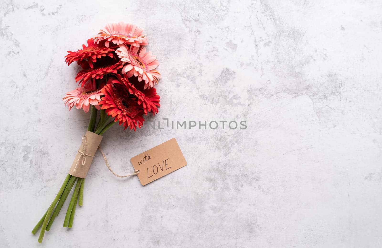 Happy birthday. Red gerbera daisy flowers and craft label tag with words With Love on concrete table, flat lay