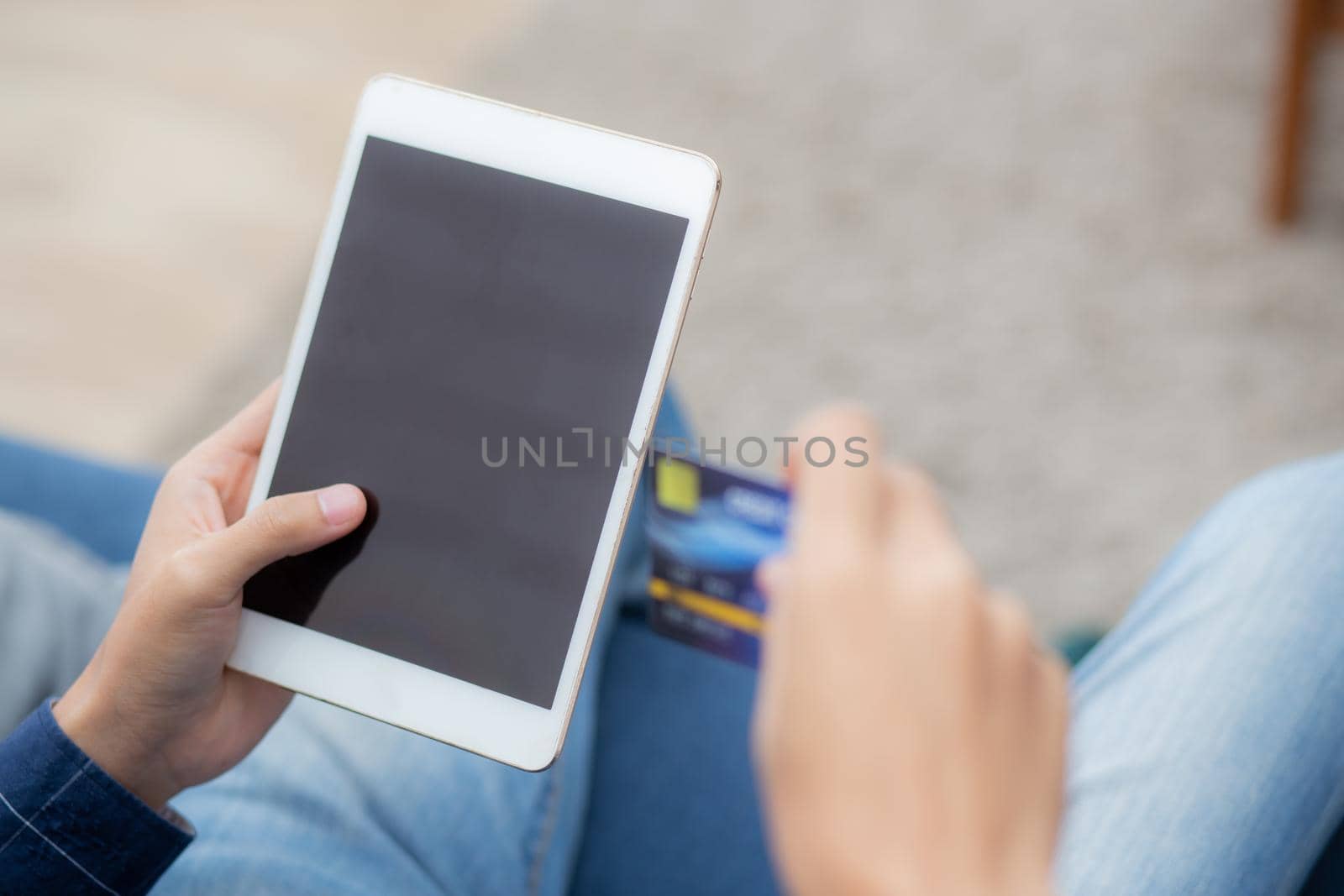 Young asian man smile holding credit card shopping online with tablet computer blank display screen buying and payment, male using debit card purchase or transaction, e-commerce concept, back view.