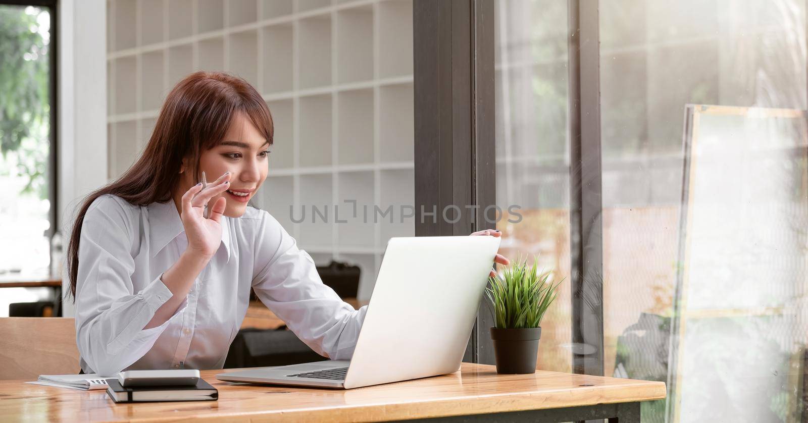 Happy asian woman smiling and waving hand at laptop, while speaking or chatting on video call in home.