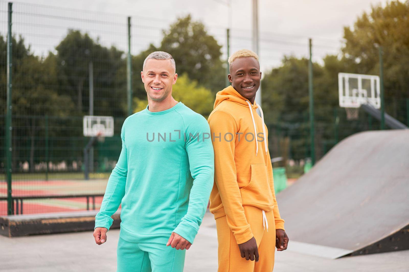 Multi-ethnic friendship Black african-american and caucasian guy friends spending time together on skate park by andreonegin