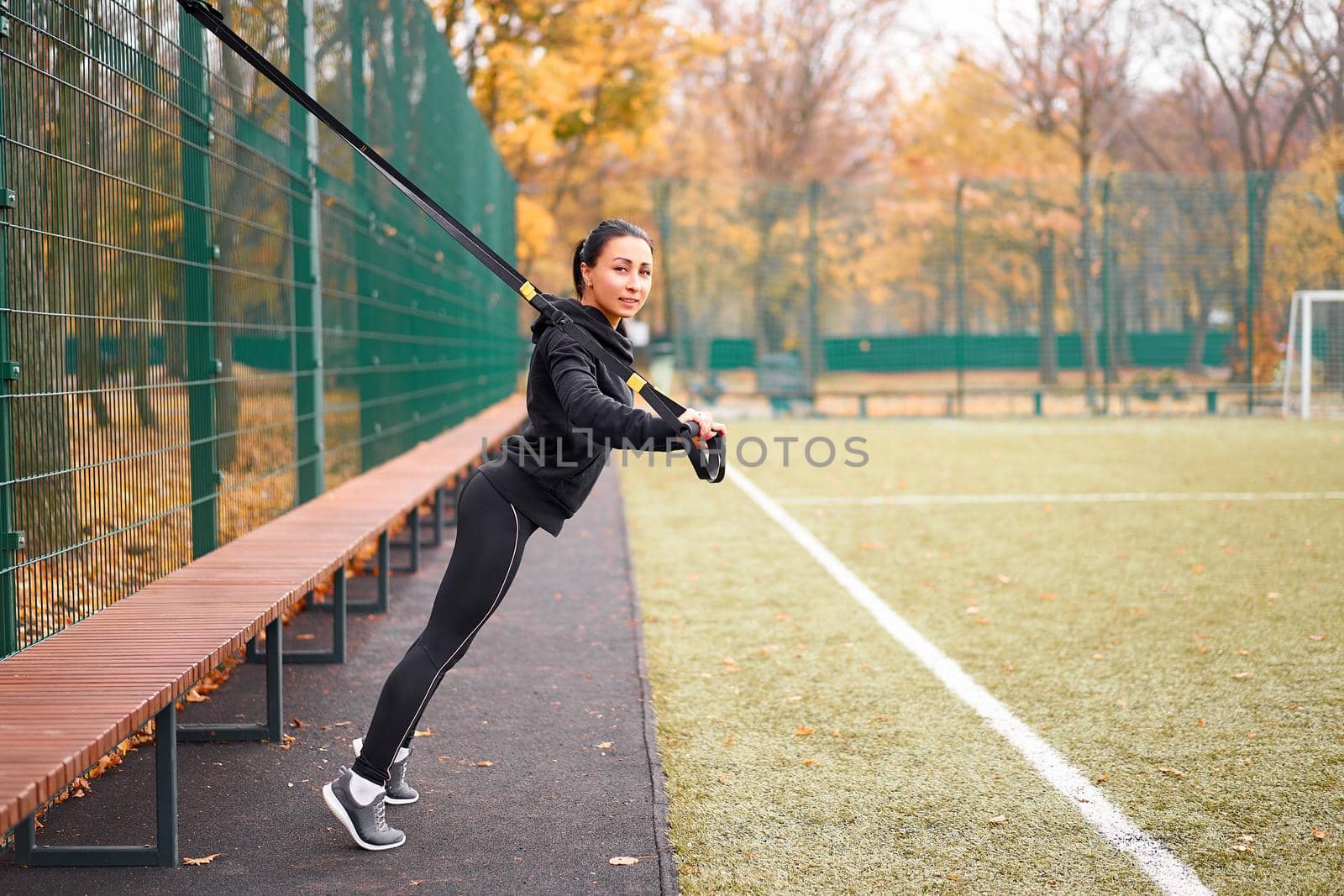 Girl athlete training using sport ground Mixed race young adult woman workout suspension system Healthy lifestyle Stretching outdoors playground. Make your body machine