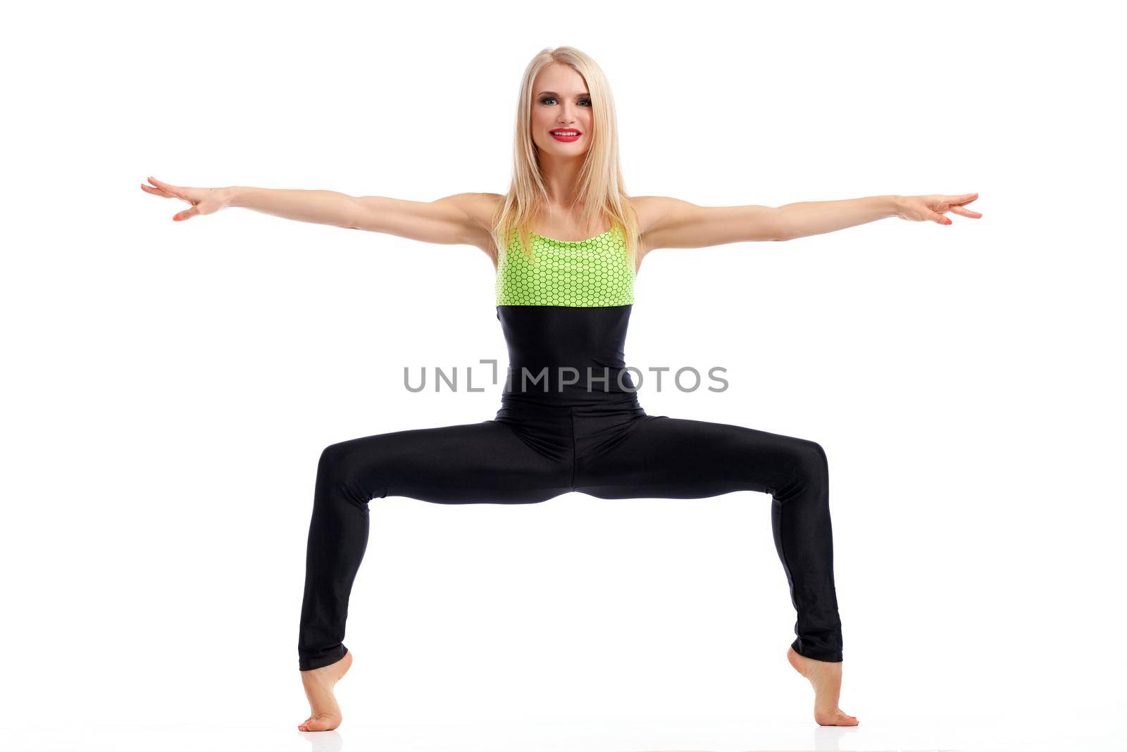 Tiptoes balance. Beautiful fit active woman smiling to the camera while doing squats balancing on her tiptoes with her arms spread to the sides isolated fitness strength squats concept