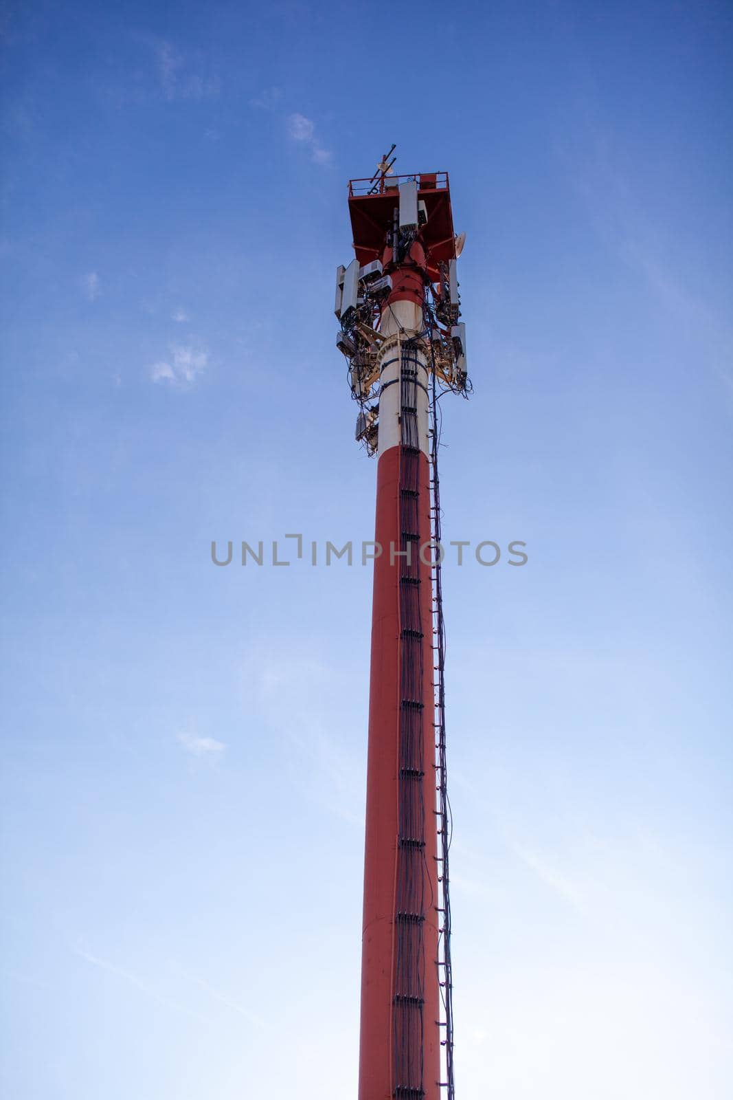 A white and red tower with cellular communication antennas on a sky by AnatoliiFoto