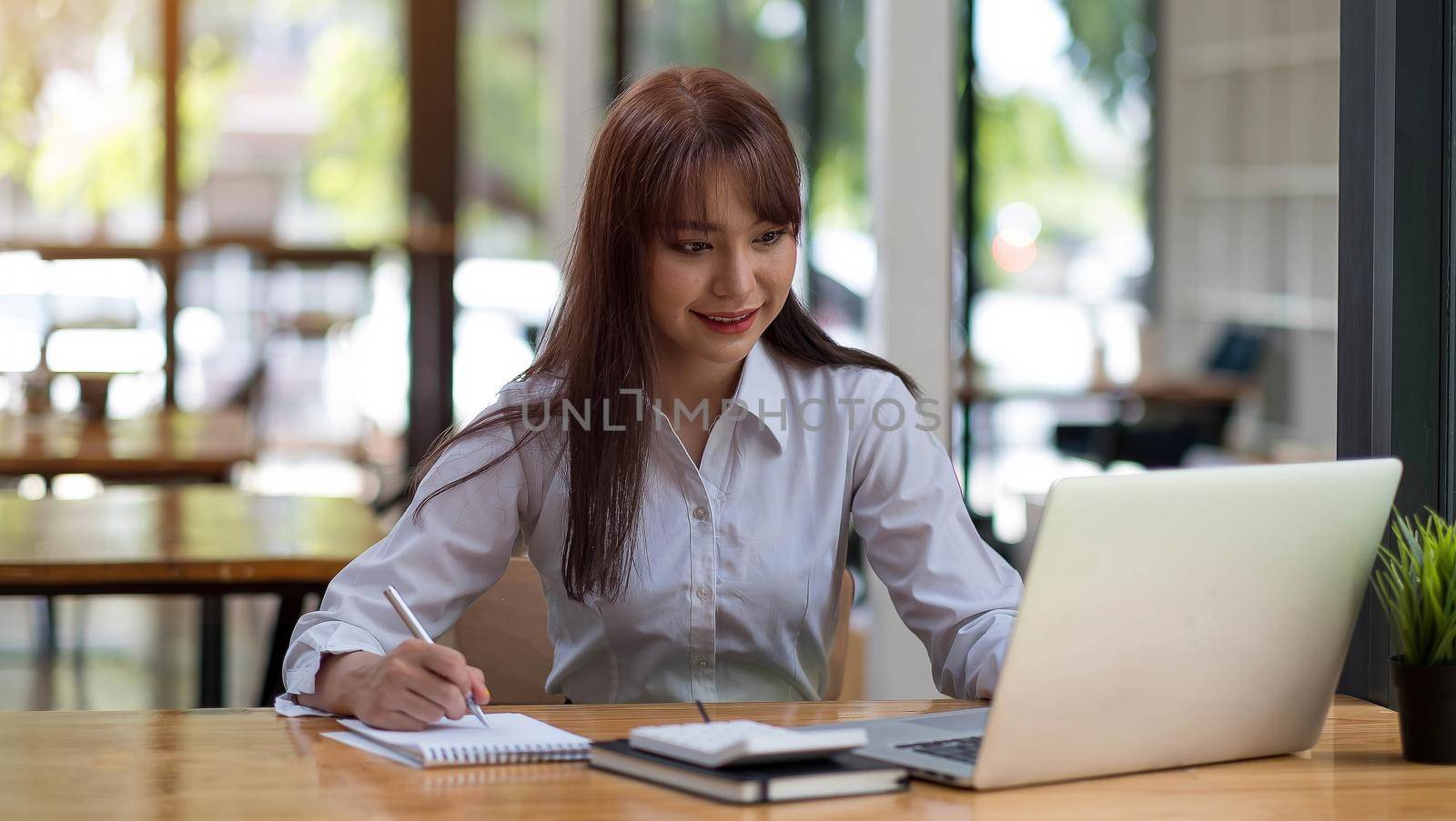 A young, cheerful girl in a white shirt smiles, smiling toothily writing down notes holding training for students to be executives at laptop desktop table